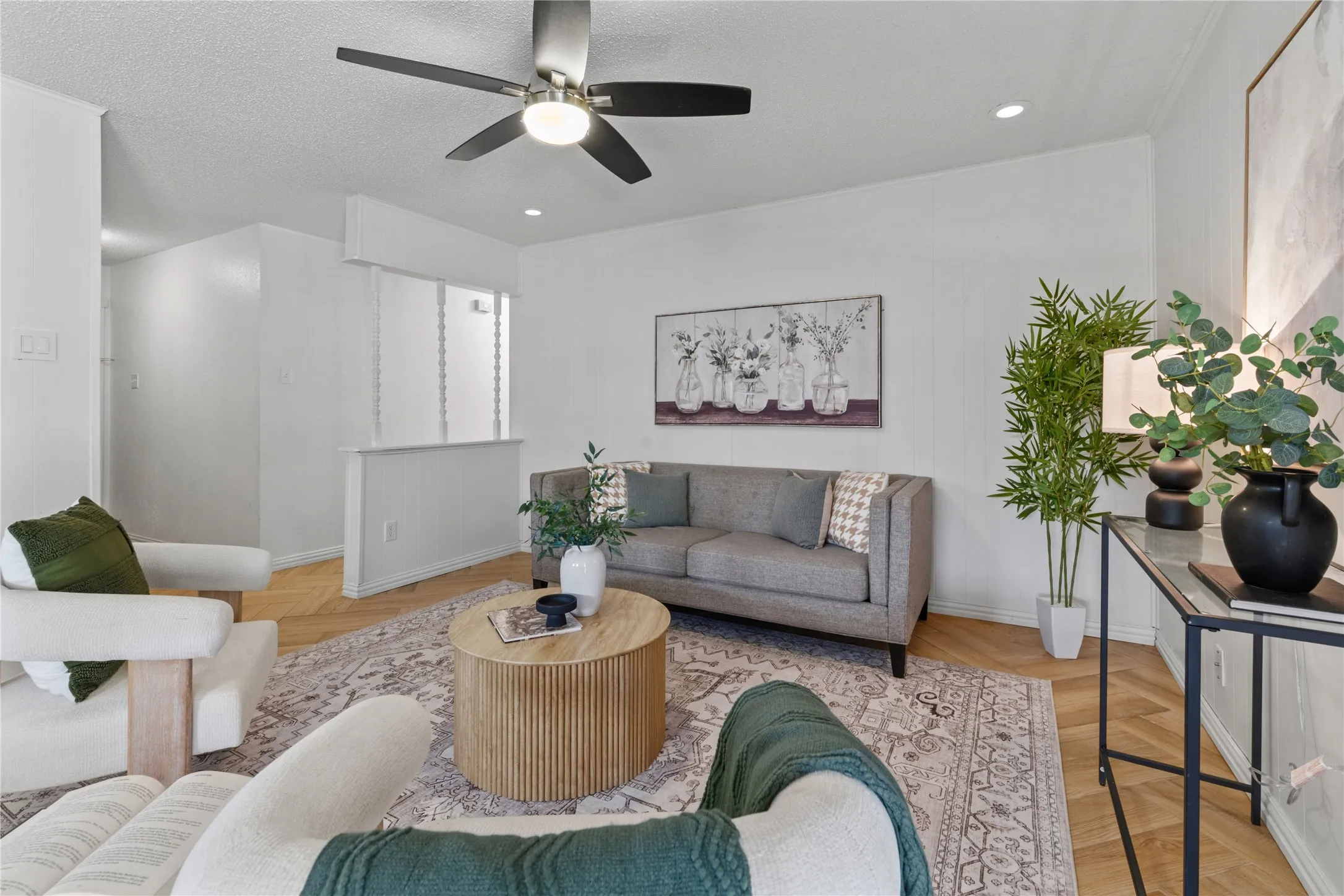 Herringbone-patterned wood-finish flooring, brushed nickel ceiling fan with integrated lighting, and a half-wall partition featuring vertical spindle accents
