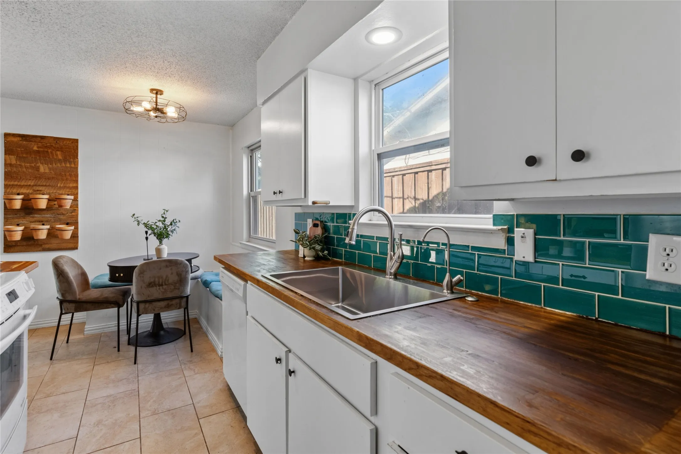 Kitchen featuring wood countertops, white cabinetry, a stainless steel undermount sink with a gooseneck faucet, a teal subway tile backsplash, and tile flooring