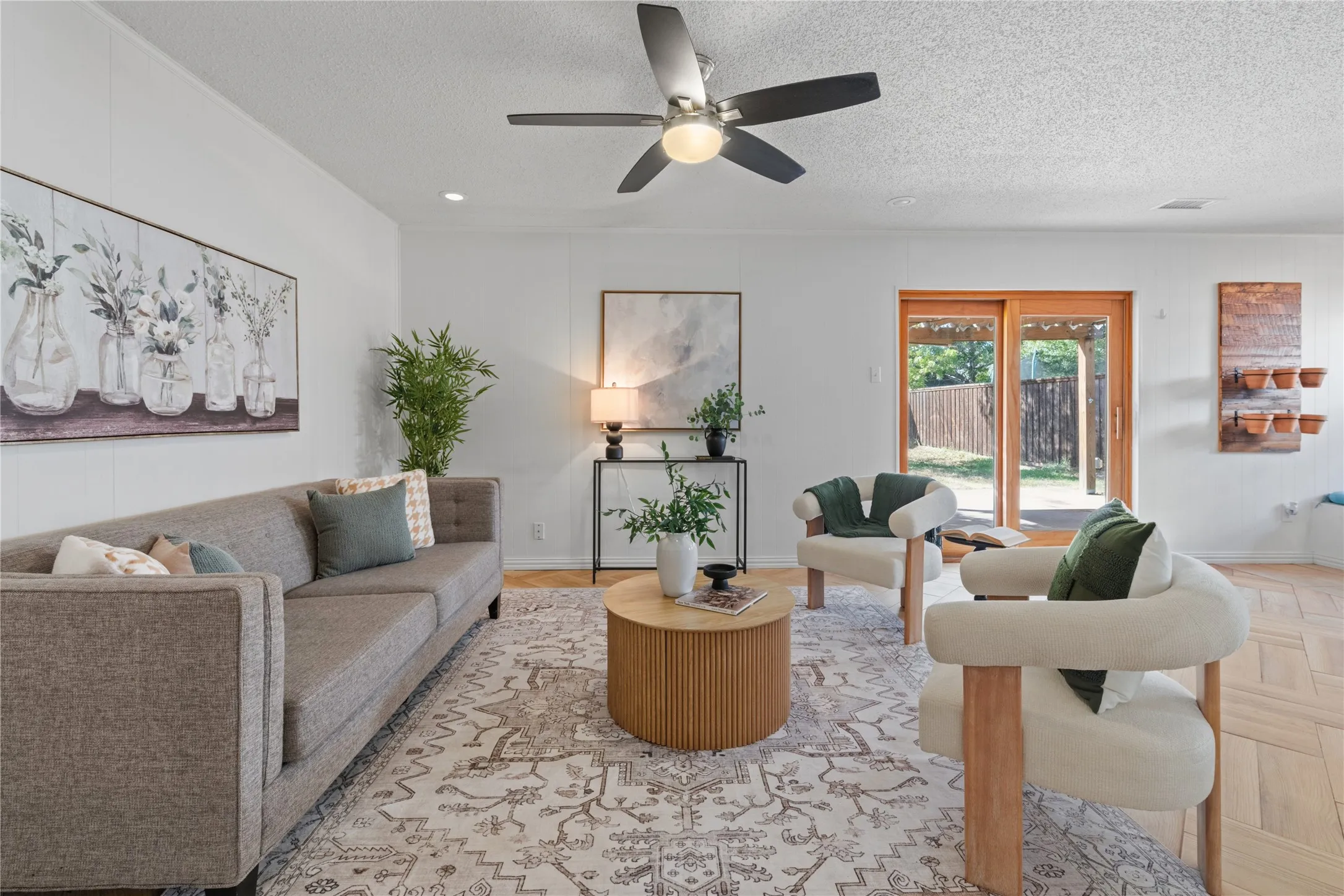Living area featuring wood-finish flooring in a herringbone pattern, a central ceiling fan with integrated lighting, and wooden-framed glass sliding doors