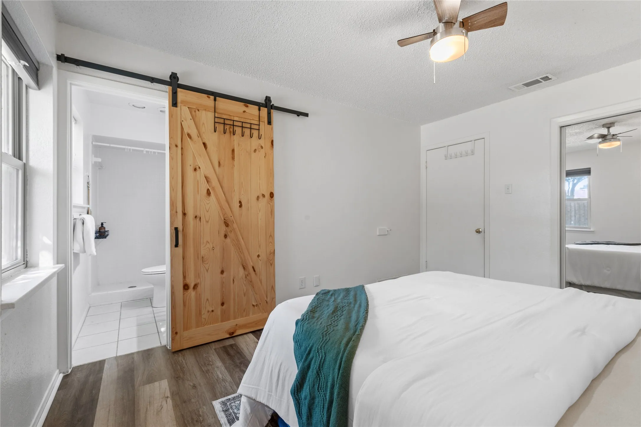 Bedroom featuring wood-finish flooring, a wood-panel barn door with matte black hardware, and a ceiling fan with integrated light fixture