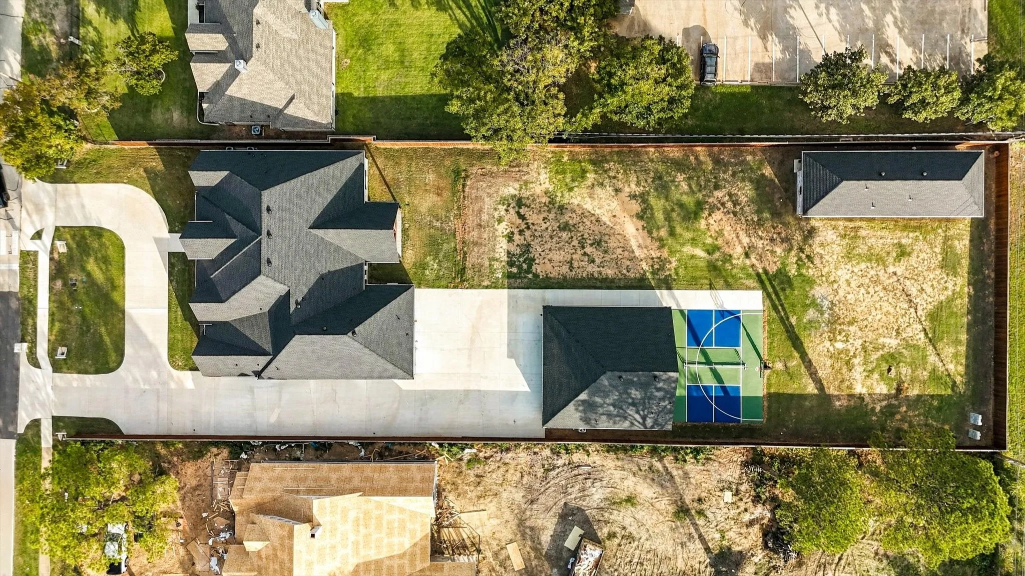 Aerial view of the property featuring a multi-pitched shingle roof, extended concrete driveway, detached secondary structure, and a hardscaped court