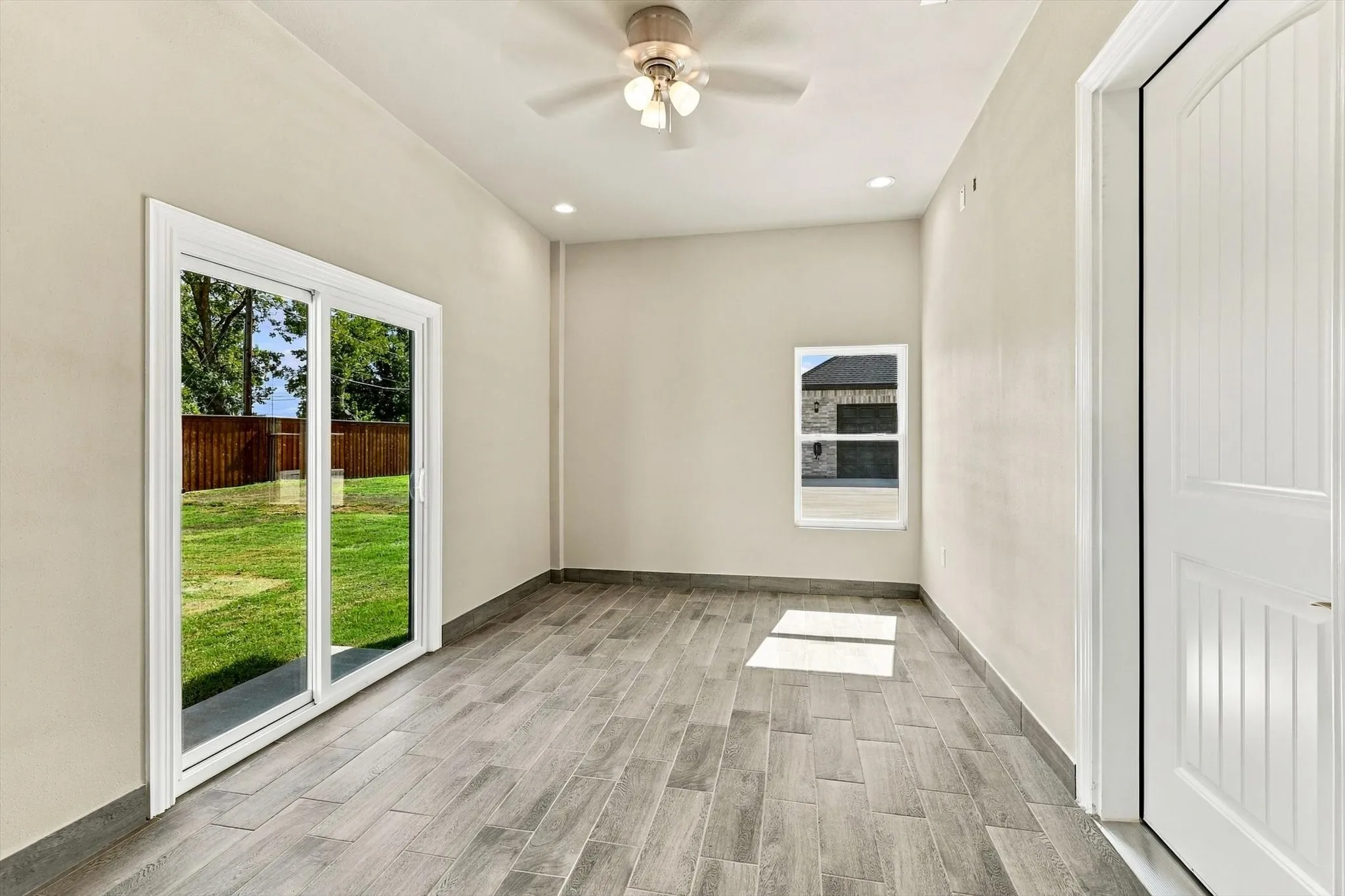 Neutral-toned interior featuring wood-finish tile flooring, recessed lighting, a ceiling fan with integrated light fixture, and a sliding glass door