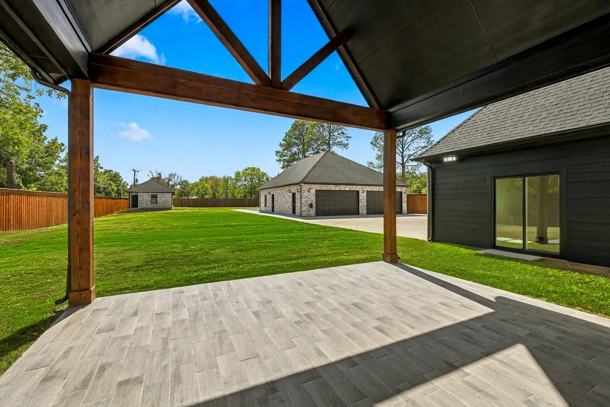 Covered patio with vaulted timber-framed ceiling, wood-finish tile flooring, and expansive grass yard