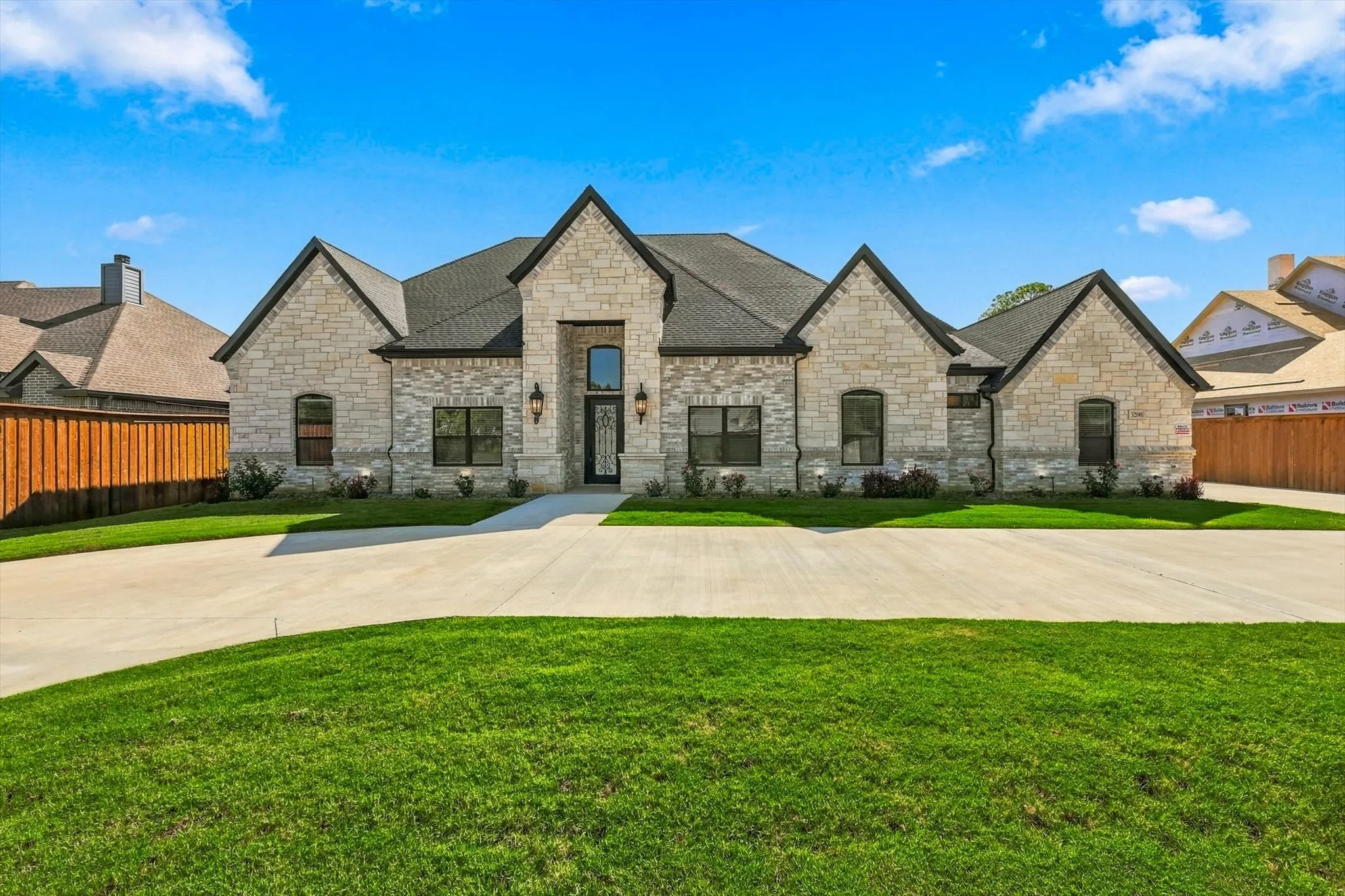 Stone exterior facade featuring a multi-gabled roofline, arched entryway with decorative glass detail, and expansive concrete driveway