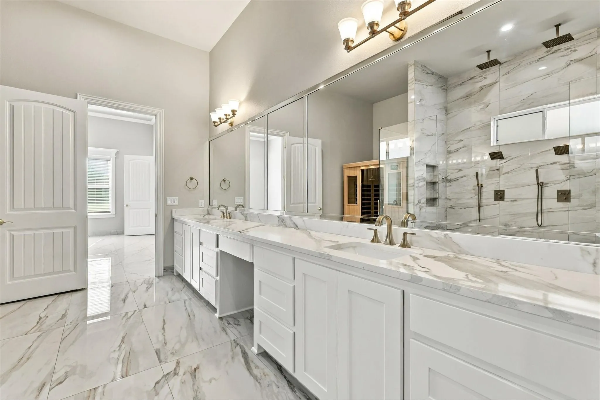 Bathroom featuring a dual-sink vanity with stone-finish countertops, full-length mirror, walk-in shower with dual shower heads, and large-format tile flooring