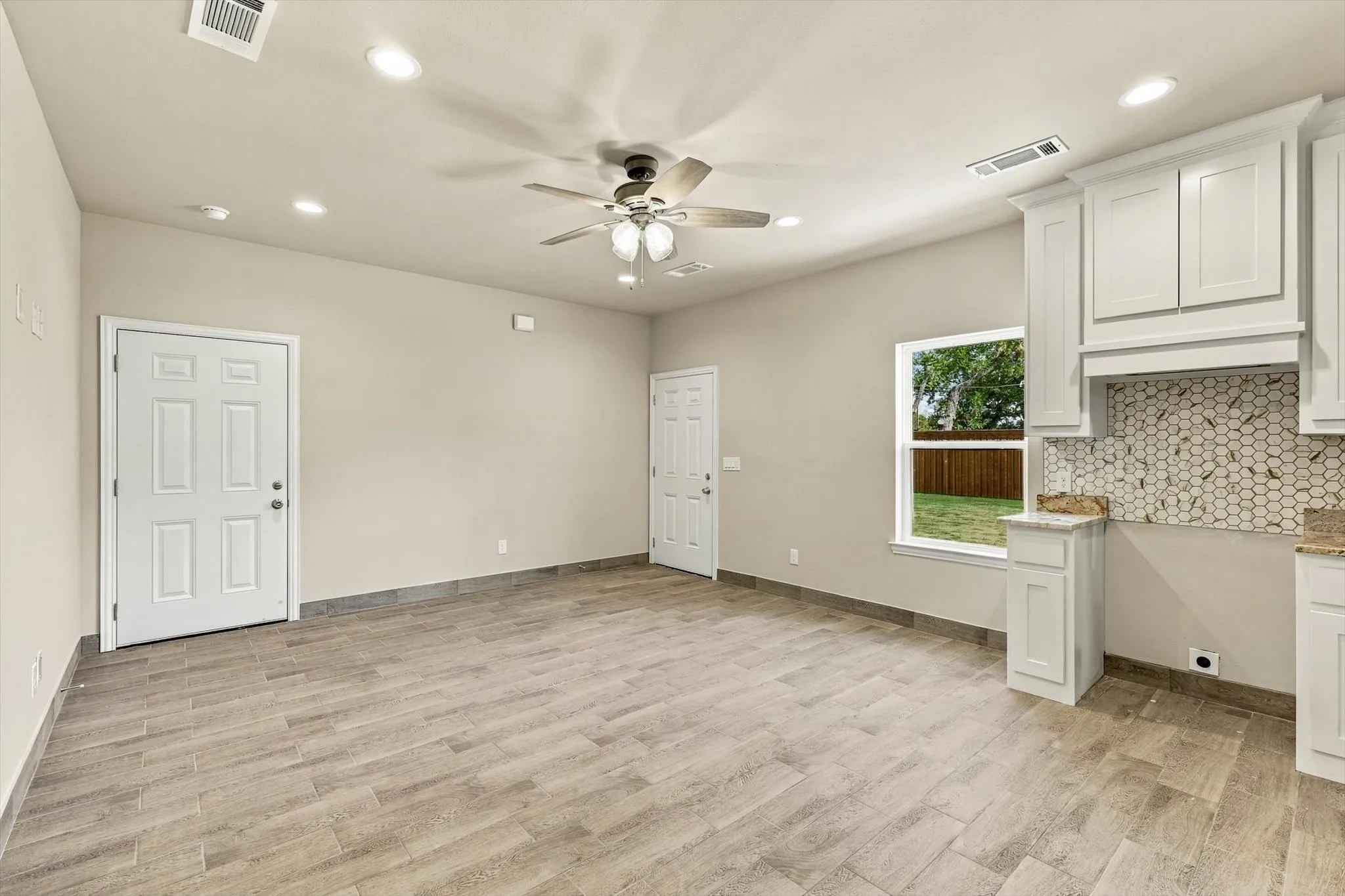 Wood-finish tile flooring, white cabinetry, hexagon-patterned tile backsplash, ceiling fan with light fixture, and recessed lighting