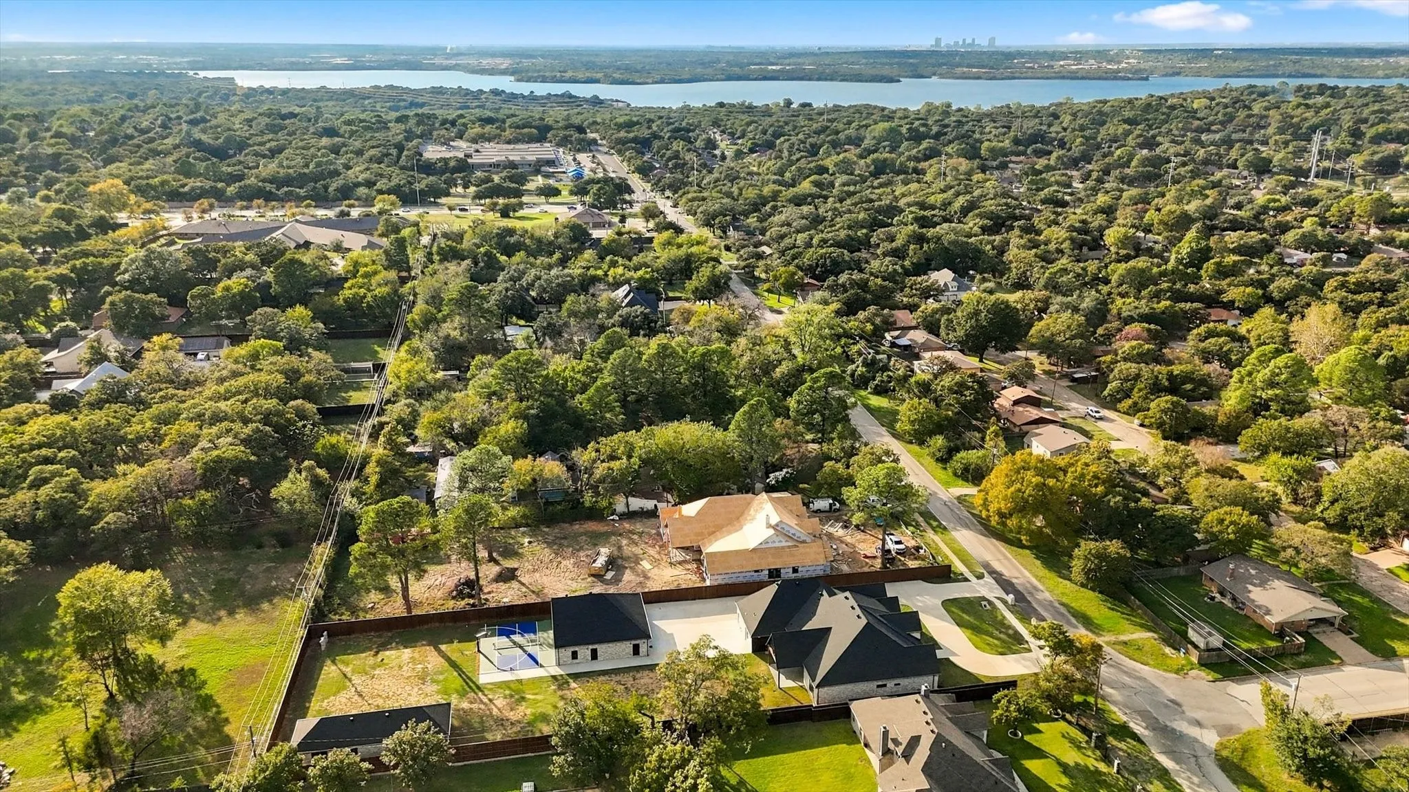Aerial perspective featuring a multi-structure property with an outdoor swimming pool, concrete hardscaping, wood-style perimeter fencing, and mature trees