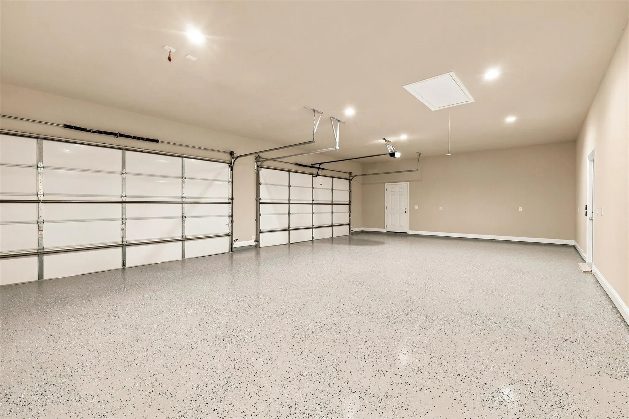 Three-car garage featuring epoxy-coated flooring, dual white sectional garage doors, recessed lighting, and an attic access hatch