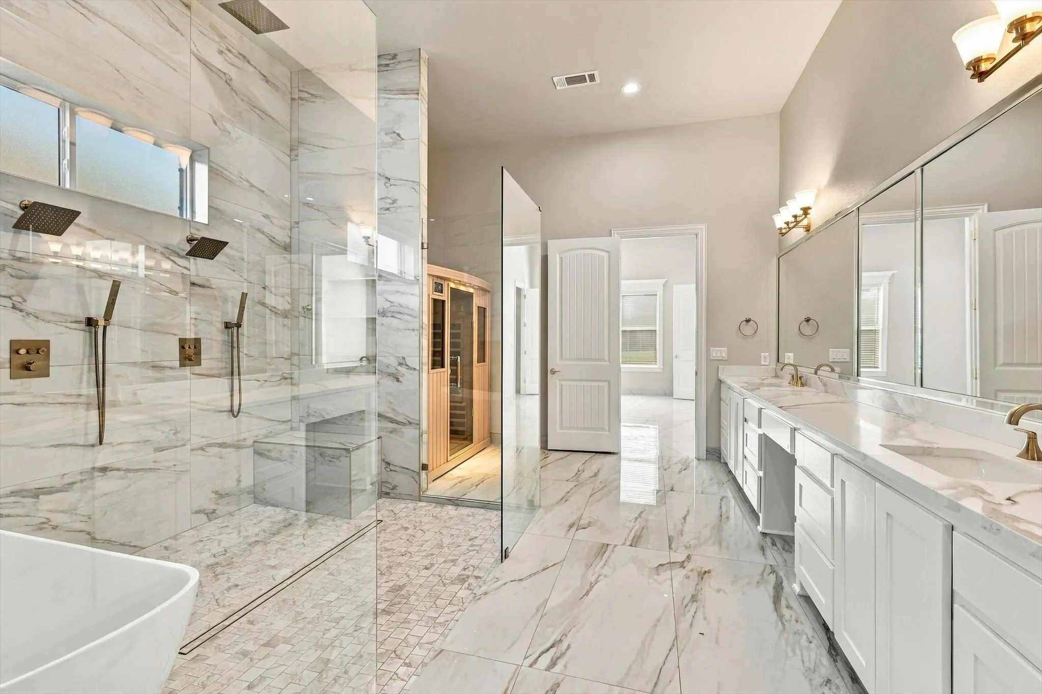 Bathroom featuring a walk-in shower with dual shower heads, a built-in sauna, stone-finish wall and floor tiling, a dual-sink vanity with stone countertops, and full-length mirrors