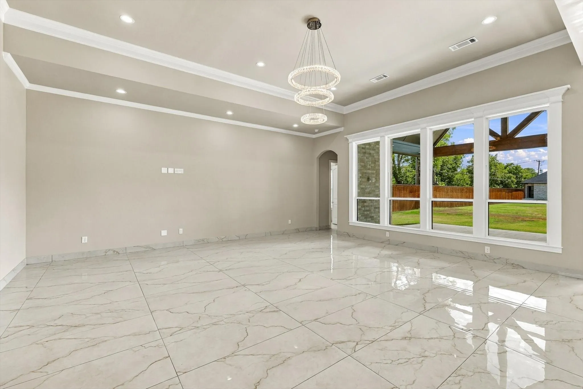 Tray ceiling with recessed lighting, large-format tile flooring, multi-tiered crystal chandelier, and expansive windows with exterior stone-accented architecture