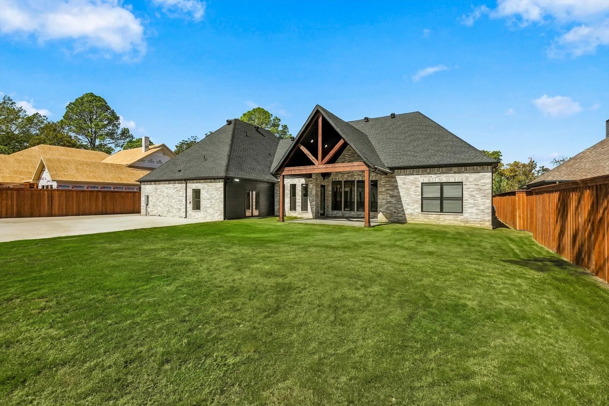 Exterior stone facade with a high-pitched roofline, covered rear patio featuring exposed timber beams, and a large grass lawn enclosed by wood fencing