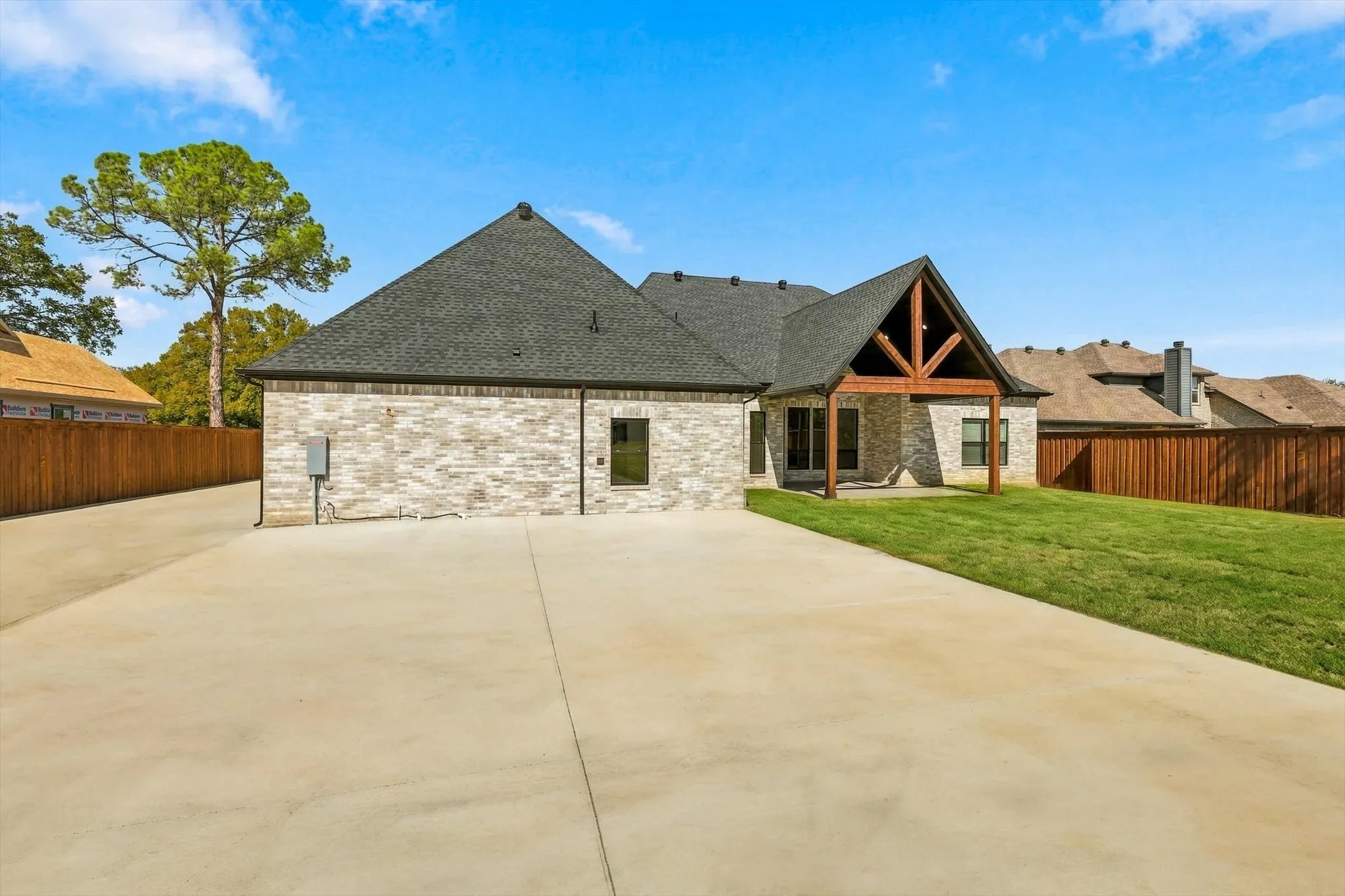 Light-colored brick exterior, covered rear patio with timber-frame accents, expansive concrete driveway, and a fenced backyard