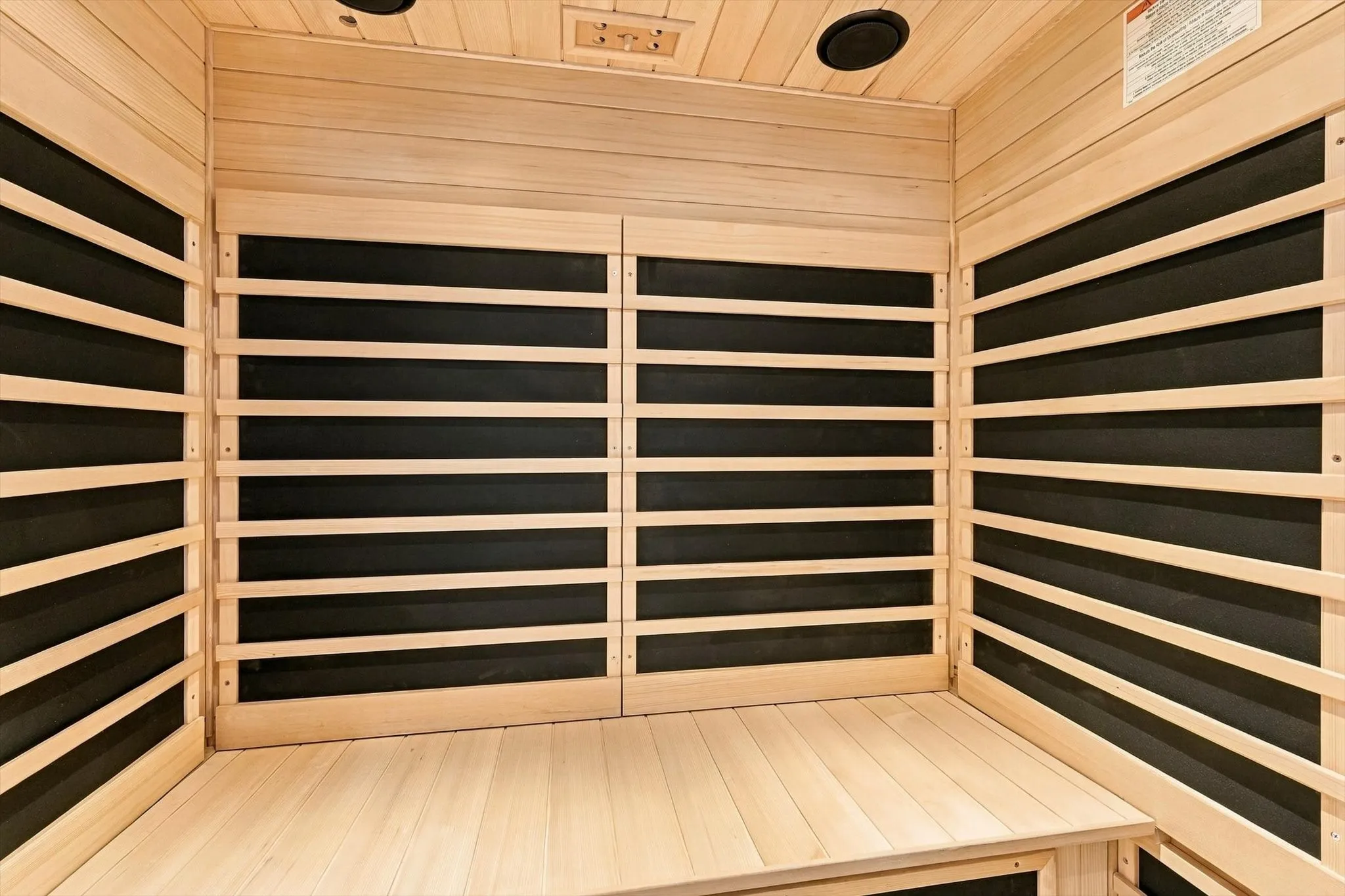 Sauna featuring light-toned wood paneling, slatted backrests, integrated ceiling speakers, and built-in bench seating