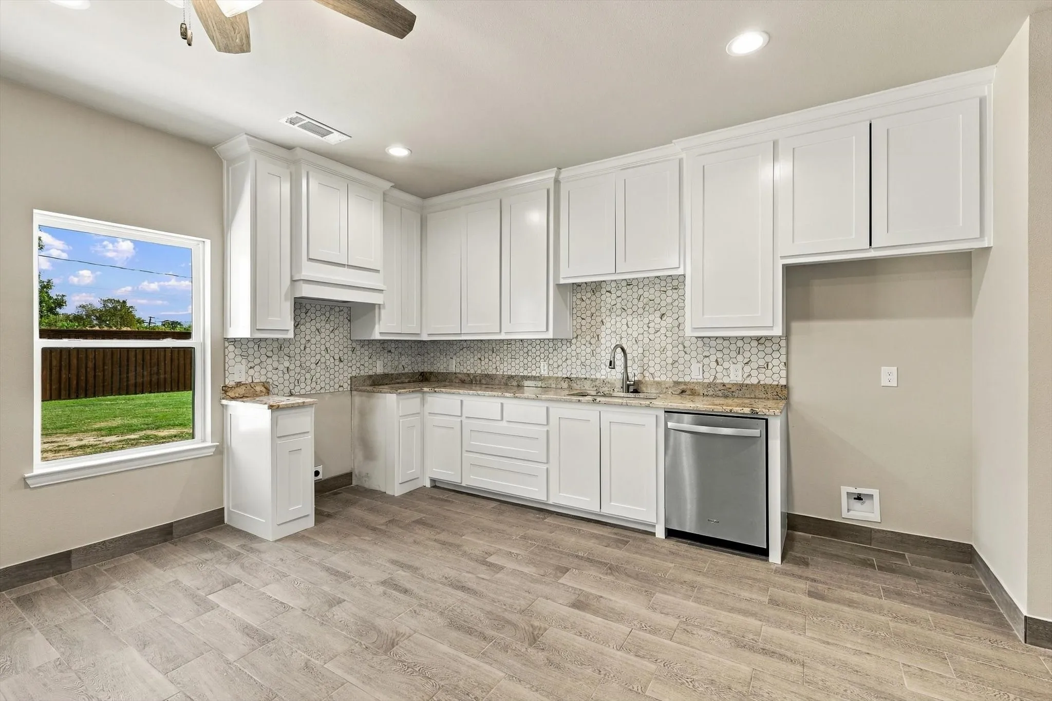 Kitchen featuring white cabinetry, stone-finish countertops, geometric tile backsplash, stainless steel dishwasher, and wood-finish flooring