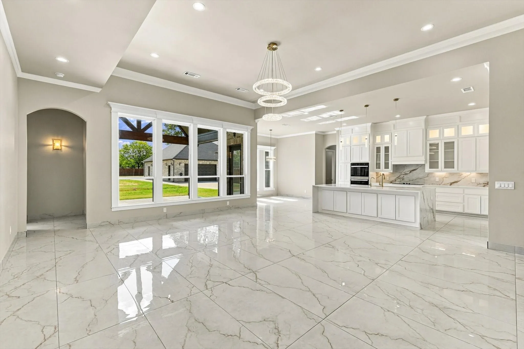 Open-concept interior featuring large-format tile flooring, a tiered chandelier, recessed lighting, and a kitchen equipped with white cabinetry and a central island
