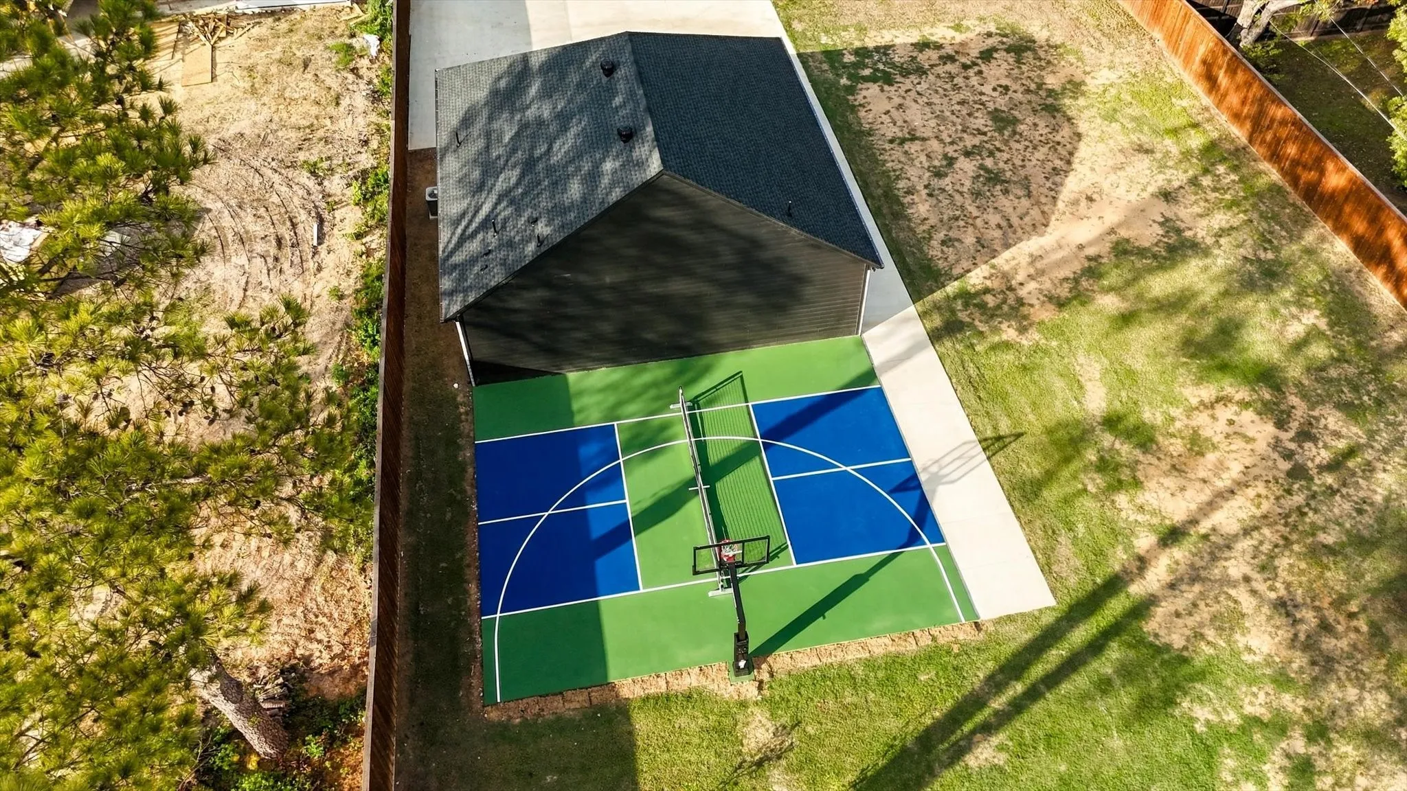 Multi-purpose sports court featuring a basketball hoop, integrated pickleball court markings, and perimeter wood fencing