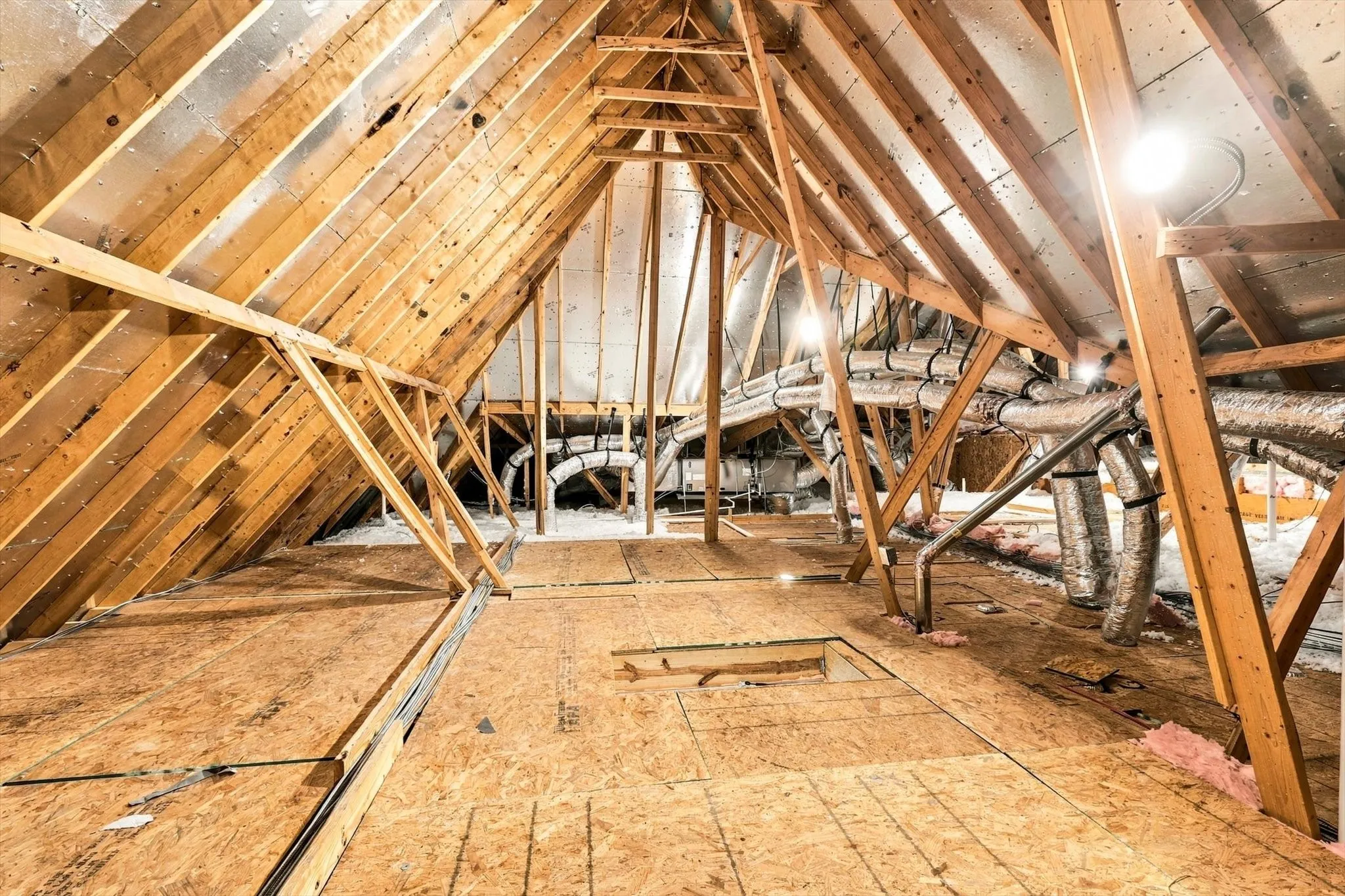 Attic space featuring wood-frame construction, exposed rafters, radiant barrier roof sheathing, plywood flooring, and integrated HVAC ductwork