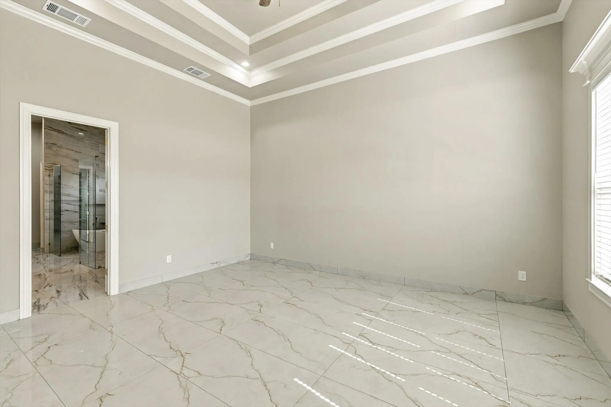 Room featuring a multi-tiered tray ceiling, large-format stone-patterned tile flooring, and crisp white crown molding