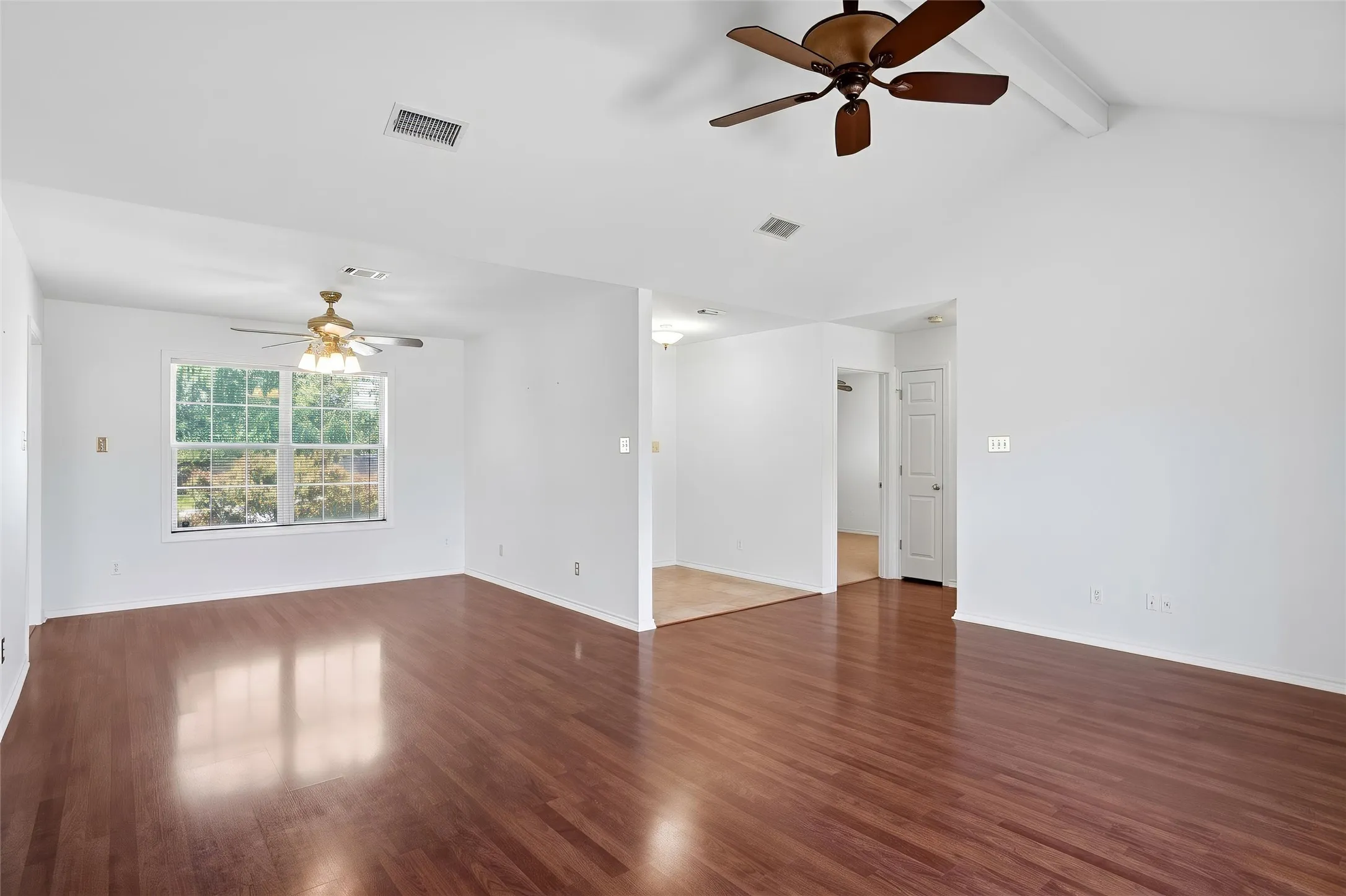 This view is looking from the family room into the dining room.  Vaulted ceiling, ceiling fan, wood-look flooring, white walls, and a large window