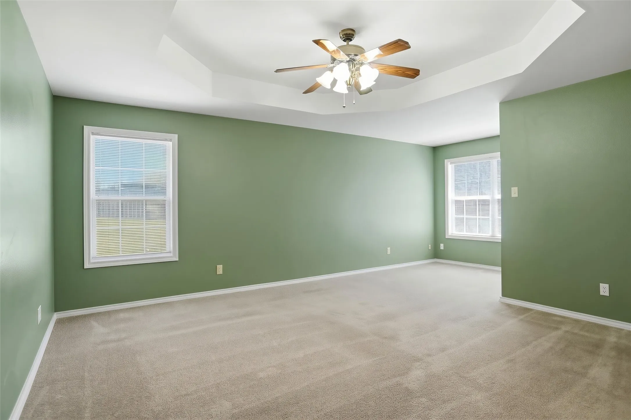 Tray ceiling with a ceiling fan, two windows, and neutral carpet