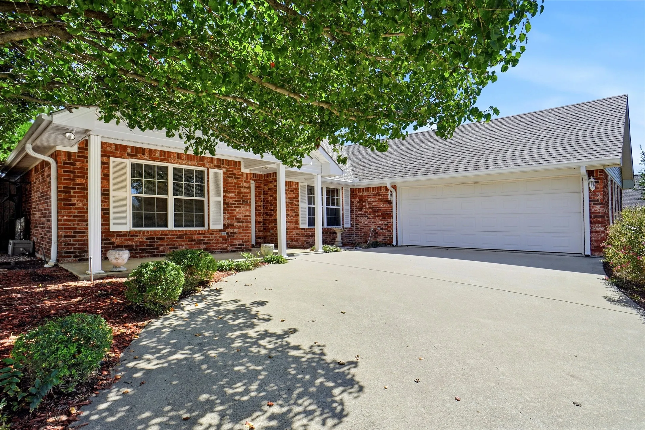 Brick exterior with white trim, a covered entryway, a concrete driveway, and an attached two-car garage