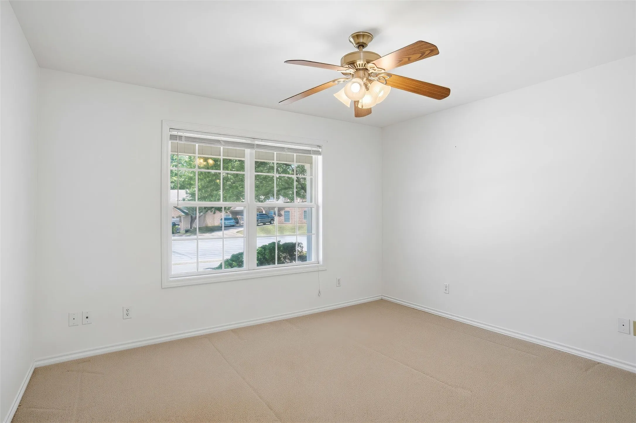 Room with neutral wall color, carpet flooring, window with white trim and ceiling fan.