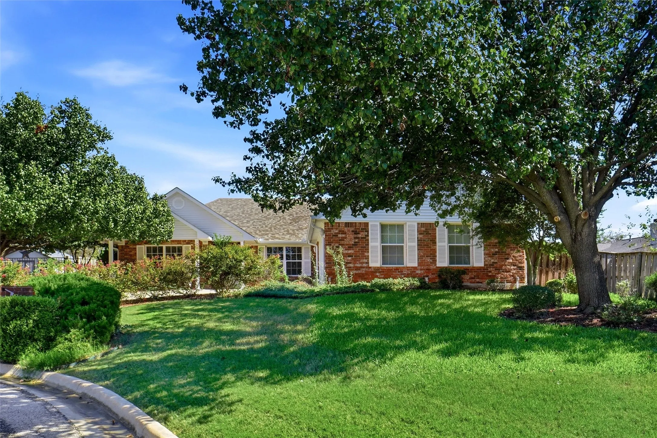 Brick exterior with white window shutters, pitched roof, and beautifully manicured lawn.