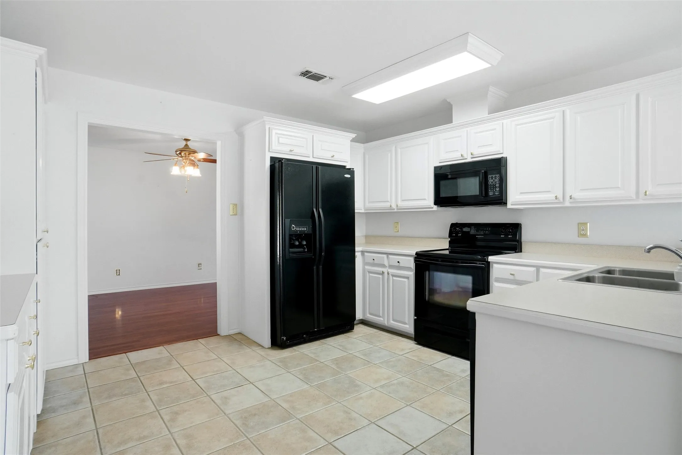 Kitchen featuring white cabinetry, black appliances, a double basin sink, and tiled flooring