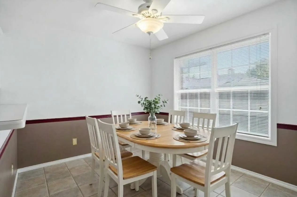 AI enhanced photo. Enjoy your morning coffee in this cheery breakfast area. Ceramic tile flooring, white walls with a contrasting accent band, and a ceiling fan with integrated lighting complete this room.