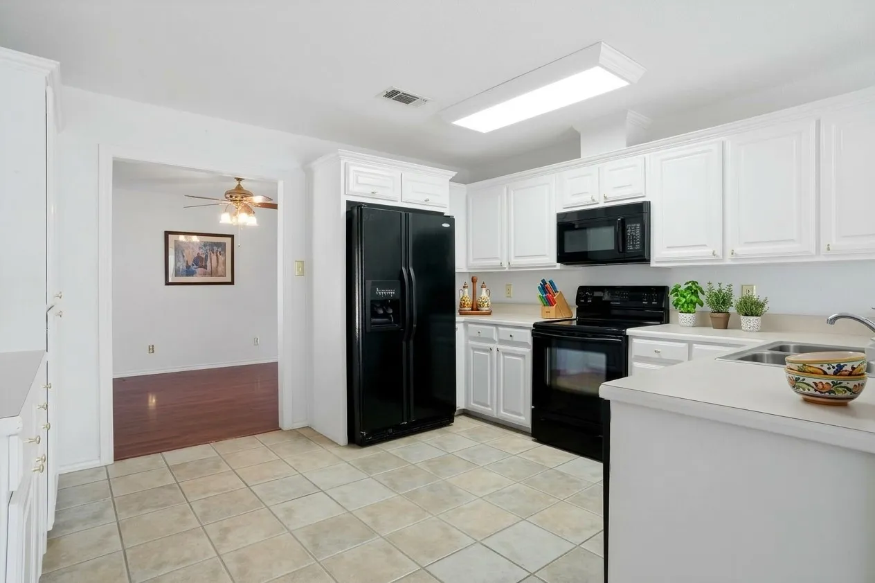 AI enhanced photo. Kitchen featuring tile flooring, white cabinetry, black appliances, and a double basin stainless steel sink.