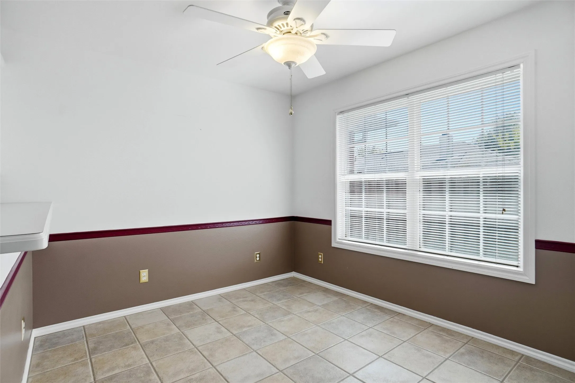 Tile flooring, overhead ceiling fan with light fixture and two-tone wall treatment.  Large window with blinds provide a lot of natural light.