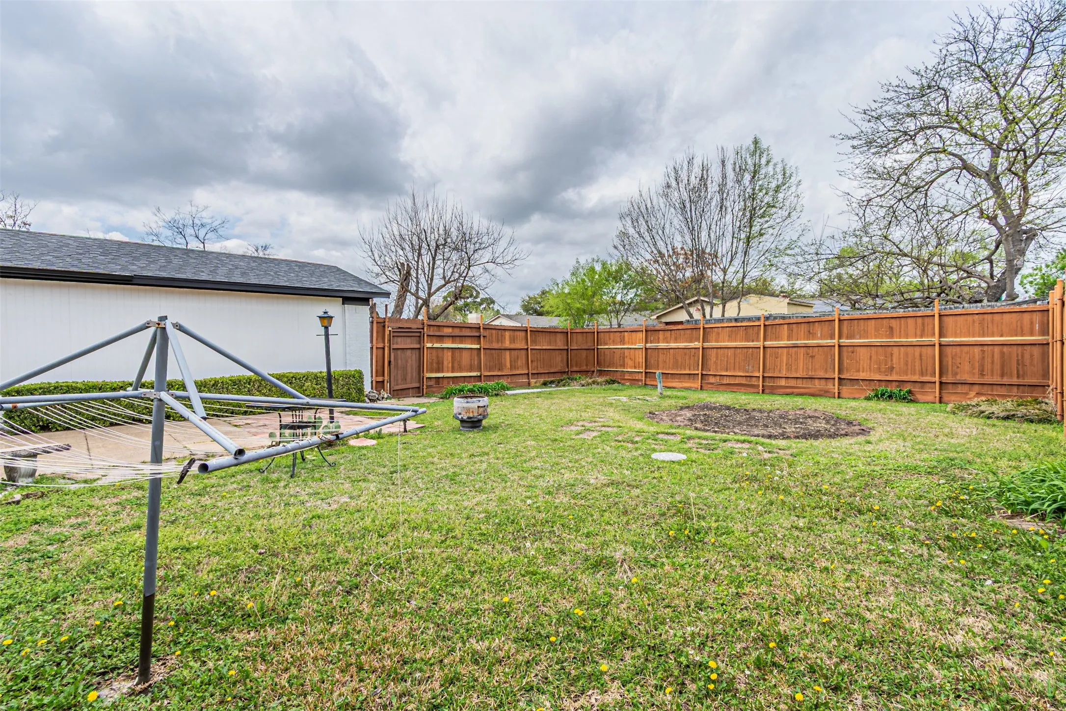 Backyard area featuring a wood-panel privacy fence, paved patio, and mature trees
