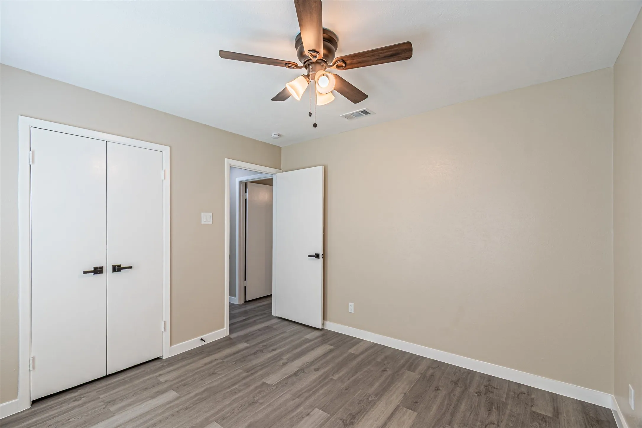 Wood-finish flooring, ceiling fan with integrated lighting, and white interior doors featuring matte black hardware