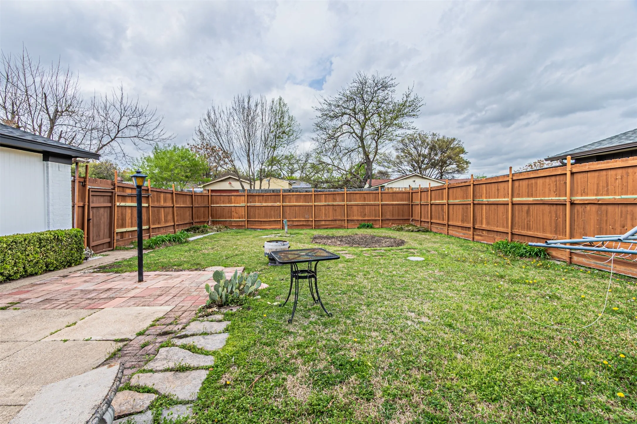Backyard featuring a wood privacy fence, brick-paved patio, flagstone pathway, and grass lawn