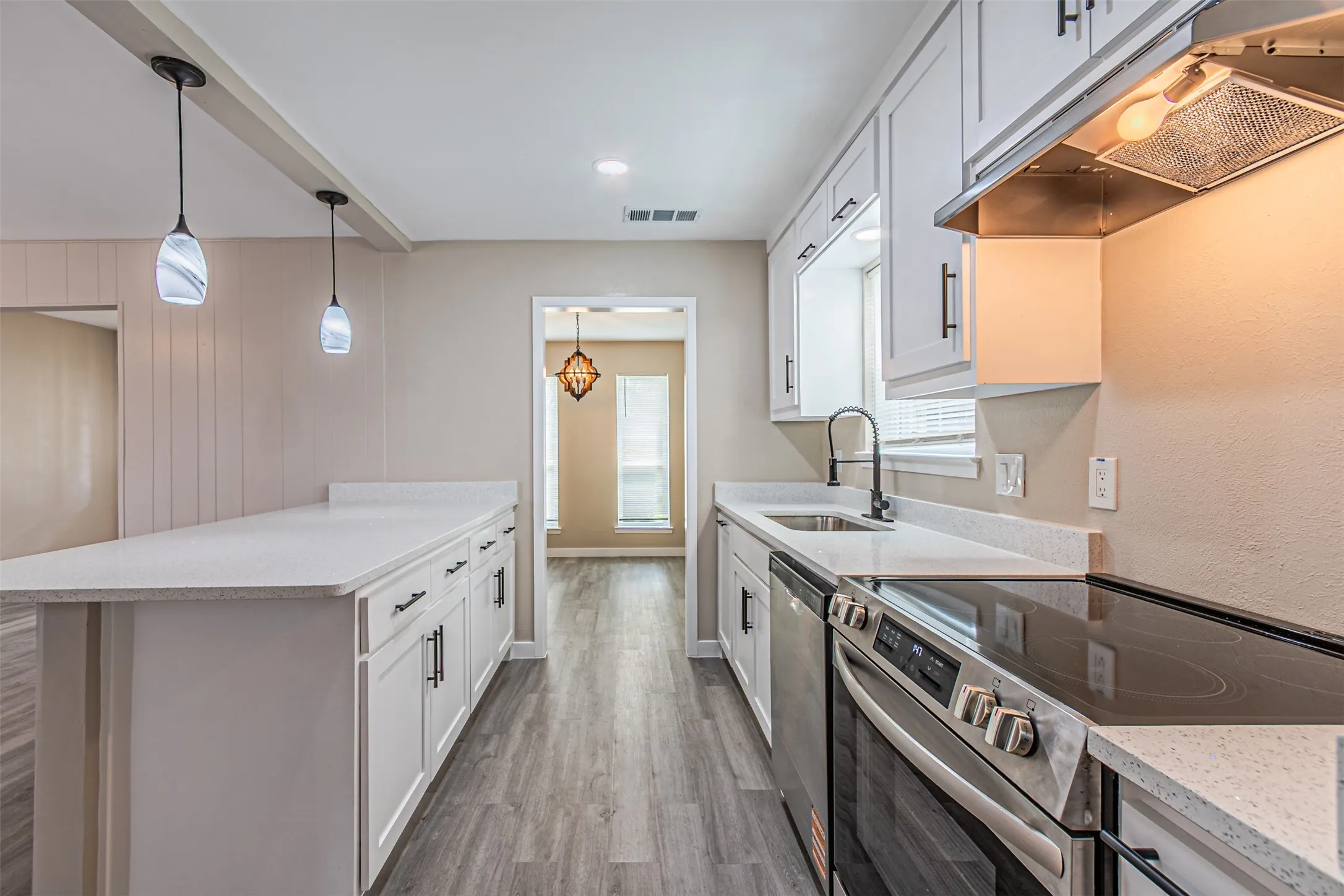 Kitchen featuring white shaker cabinetry, stone-finish countertops, stainless steel appliances, wood-finish flooring, and dual pendant lighting