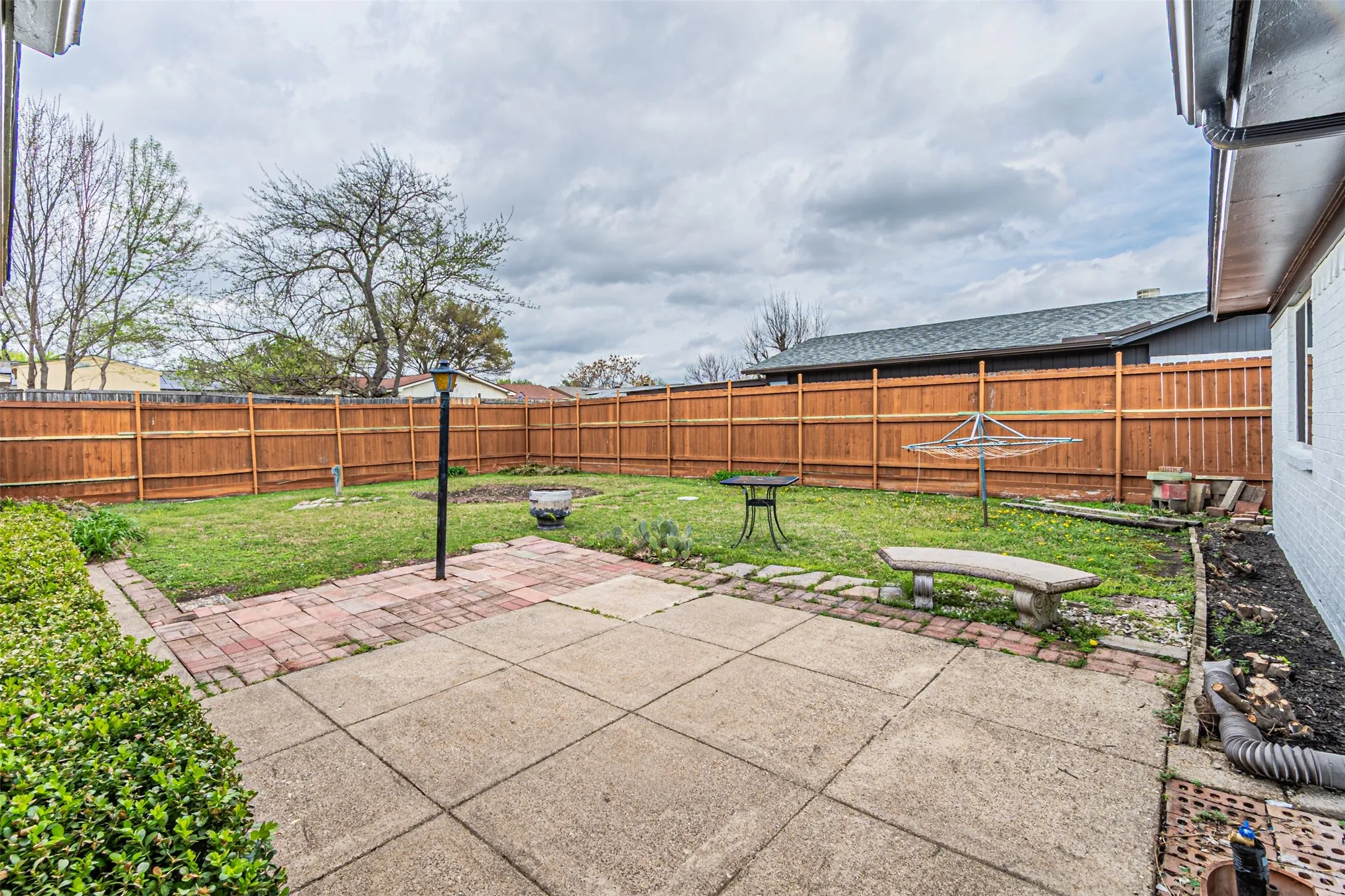 Backyard featuring a concrete patio, brick hardscaping, a wood privacy fence, and mature landscaping