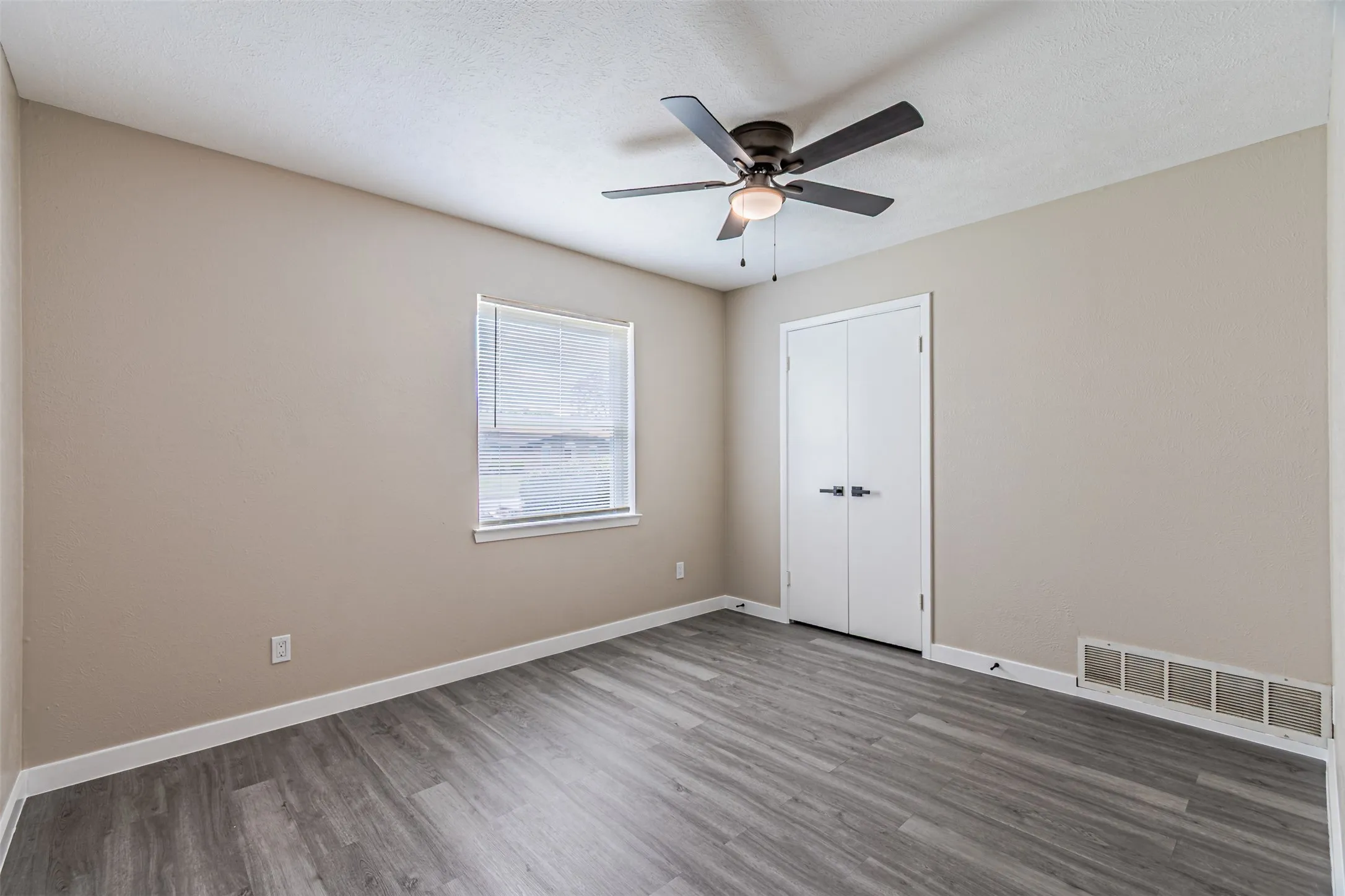 Neutral wall finishes, wood-finish flooring, ceiling-mounted light fixture with fan, and double-door closet