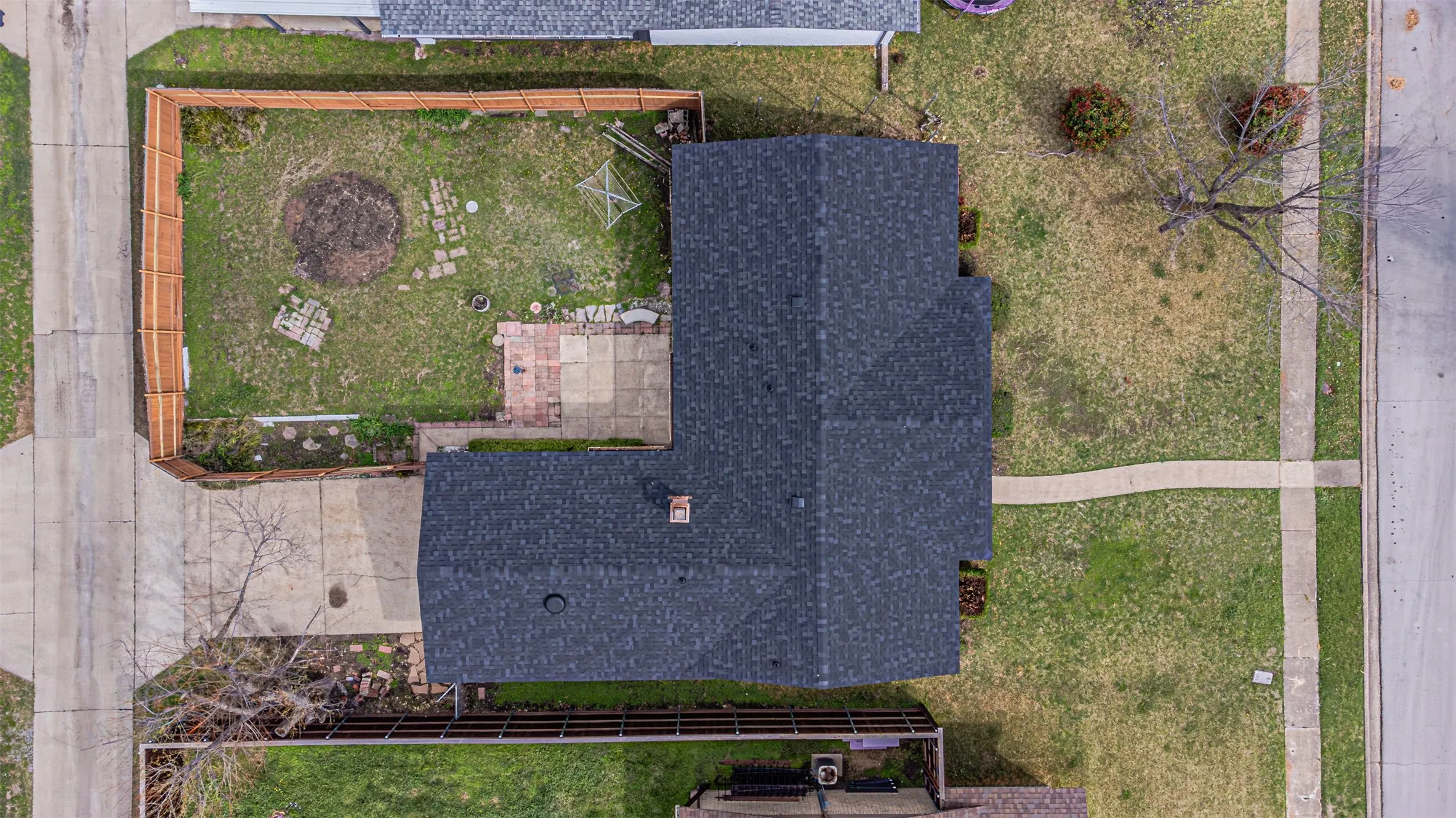 Aerial view featuring a fenced-in rear yard, concrete patio, asphalt shingle roof, and paved driveway