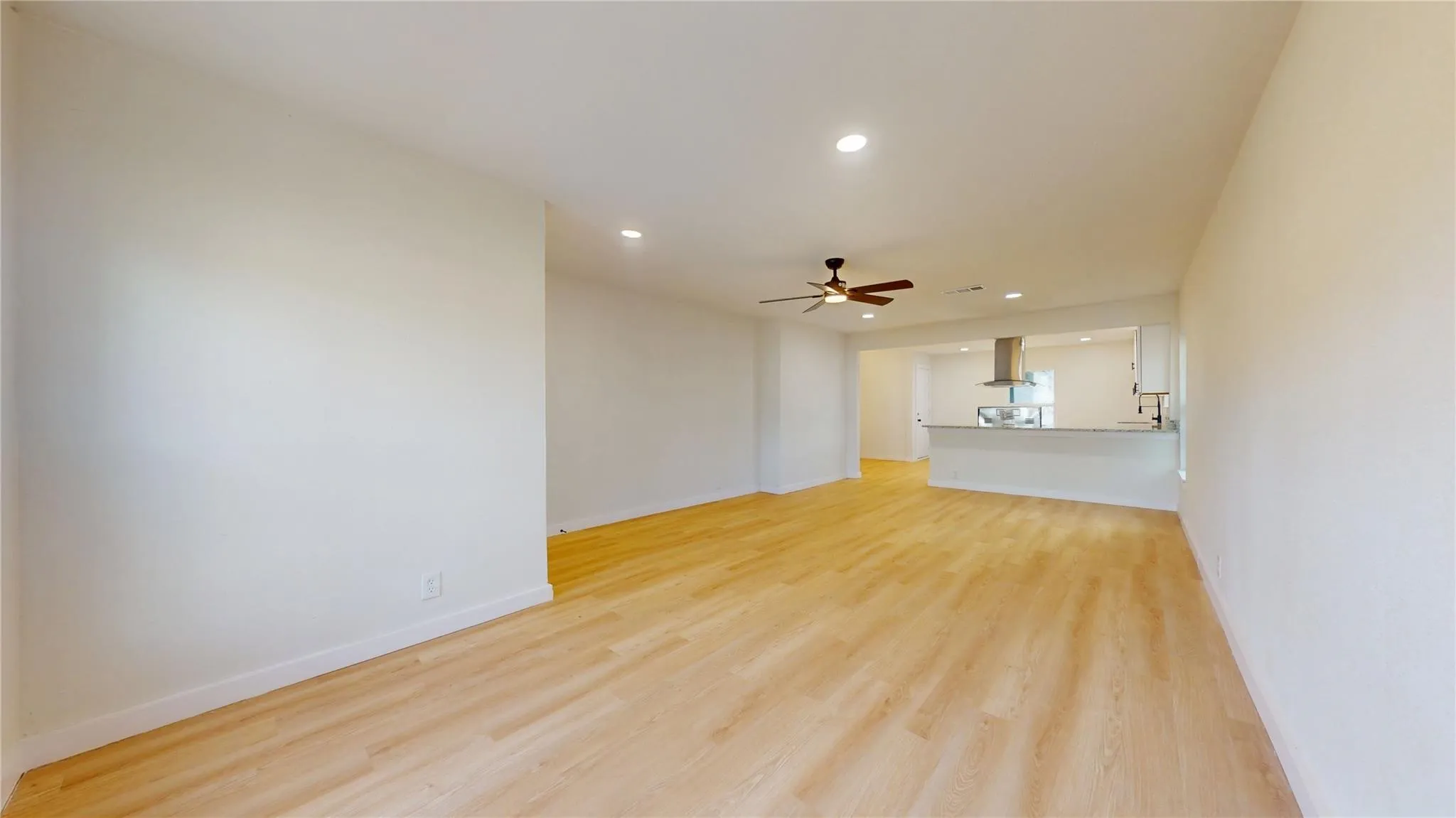 Open floor plan featuring wood-finish flooring, recessed lighting, ceiling fan, and a breakfast bar with a stainless steel range hood