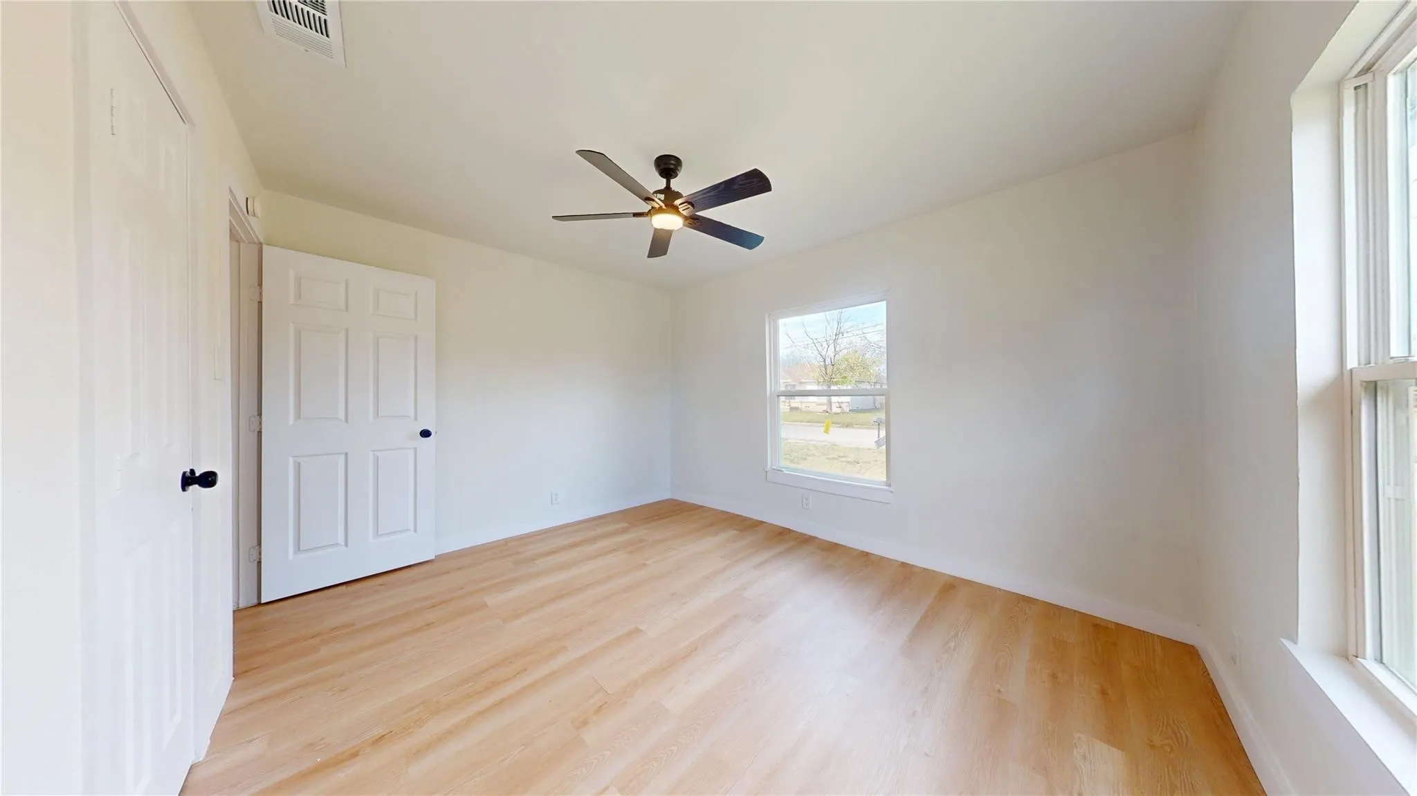 Neutral-toned room featuring wood-finish flooring, a ceiling fan with integrated lighting, dual-panel interior doors, and multiple windows