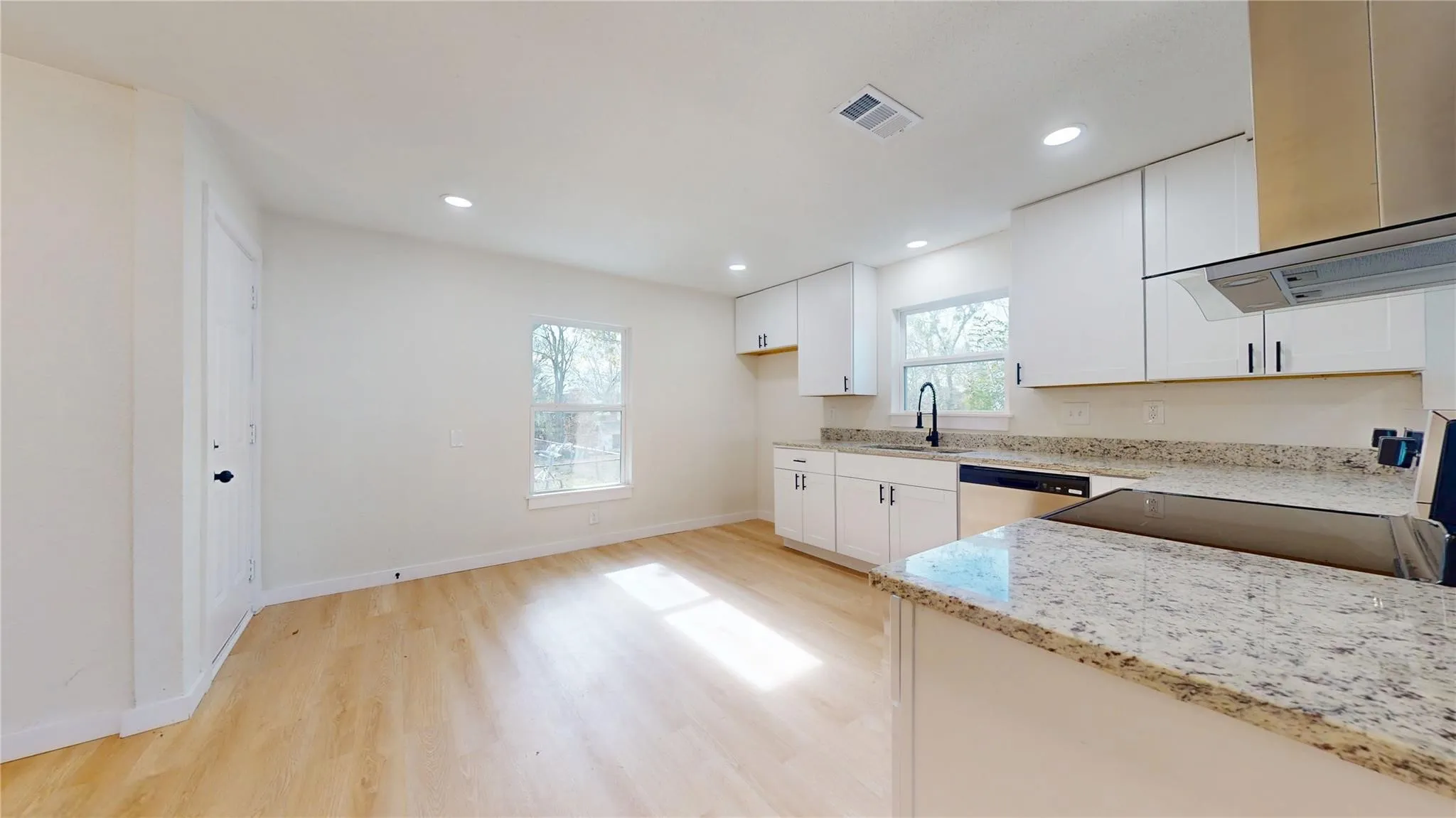 Kitchen featuring white shaker-style cabinetry, stone countertops, integrated stainless steel appliances, a matte black faucet, and wood-finish flooring