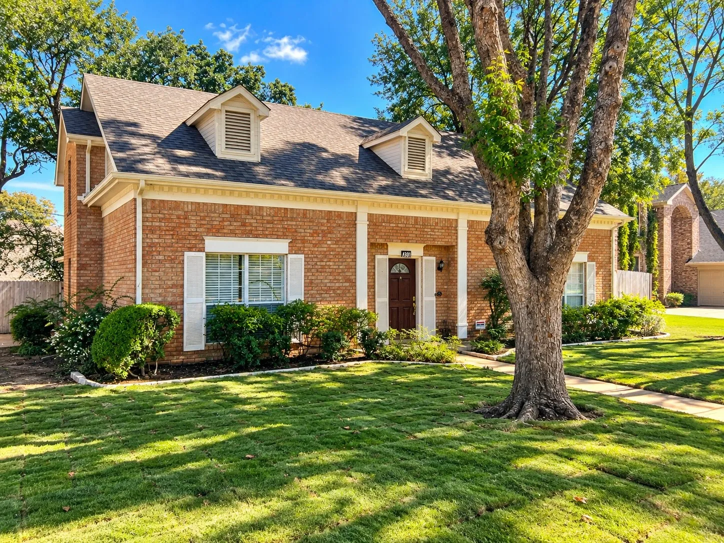 Brick exterior featuring dormer windows, architectural shingle roofing, white column detailing, and decorative window shutters