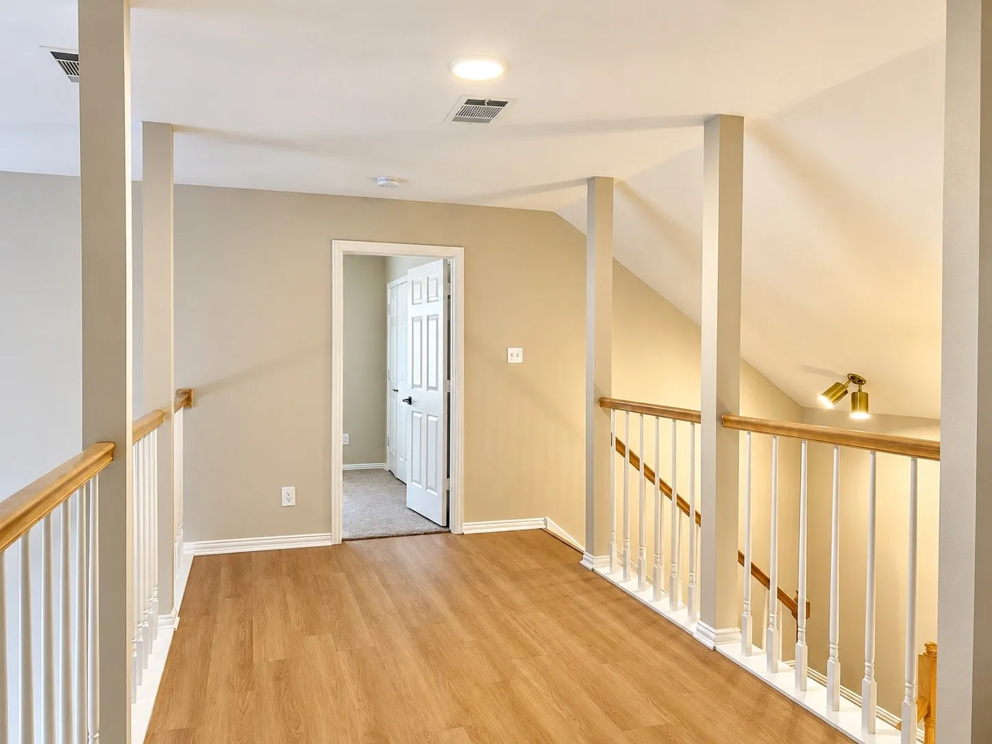 Wood-finish flooring, vaulted ceiling, and white balustrade railing with natural wood handrail