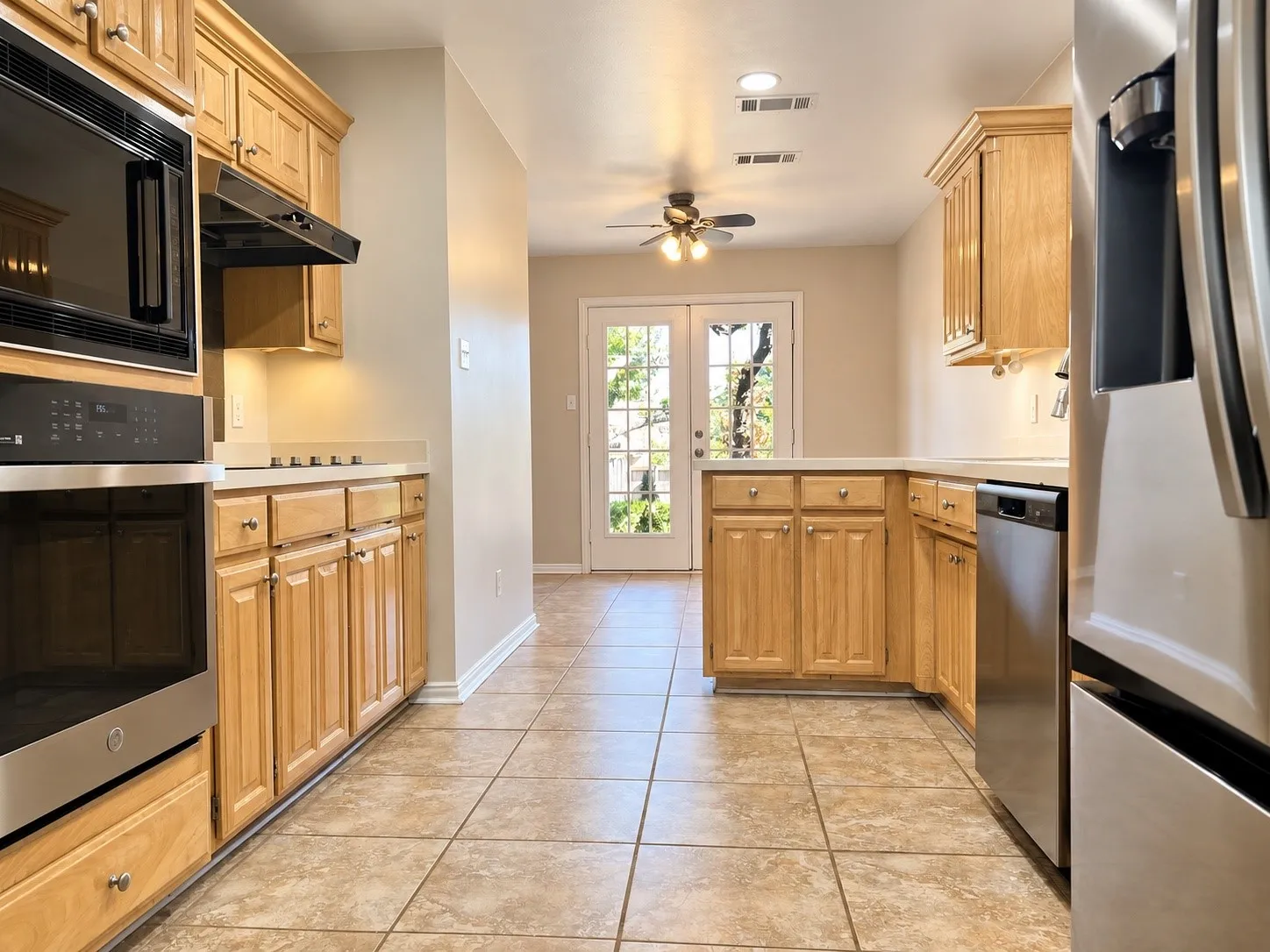 Kitchen featuring light-tone wood cabinetry, stainless steel appliances, tile flooring, and glass-paned double doors