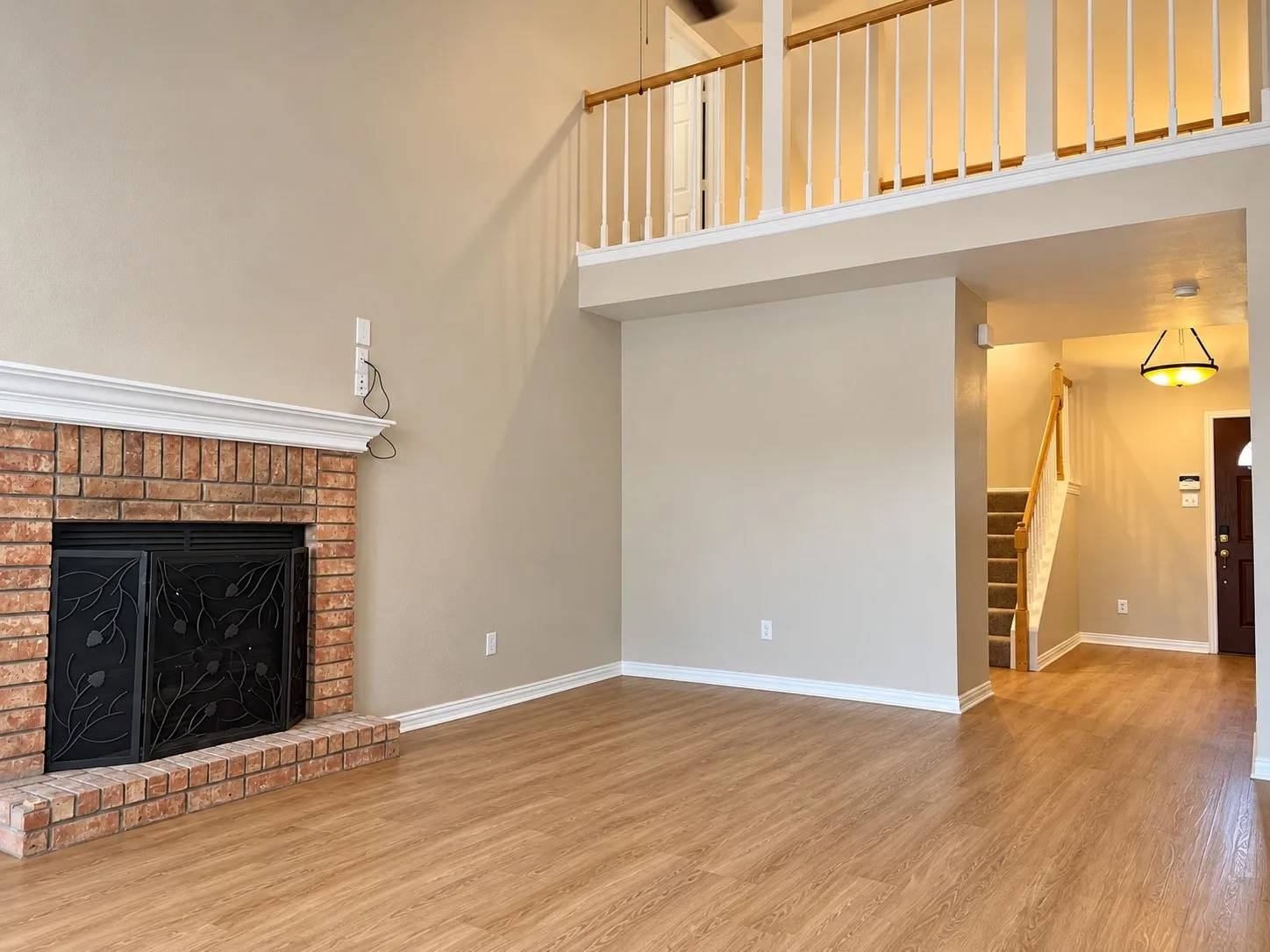 High vaulted ceilings featuring an open loft overlook with white railing, floor-to-ceiling brick fireplace with a wood mantel, and wood-finish flooring