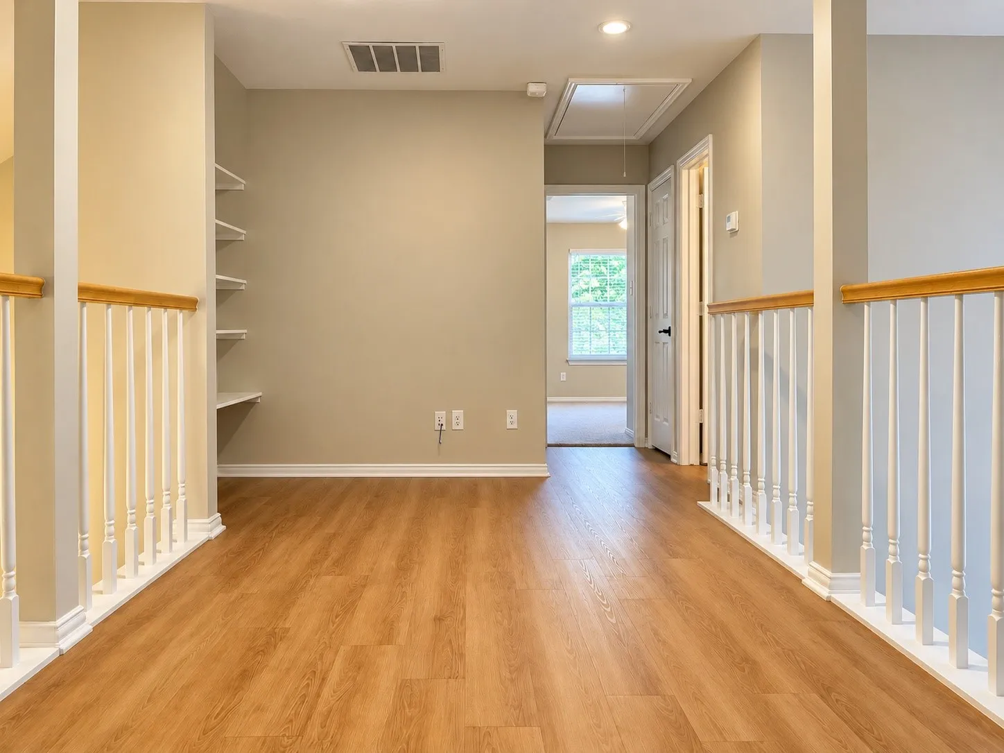 Wood-finish flooring, built-in wall shelving, and staircase railings with white balusters and wood-finish handrails