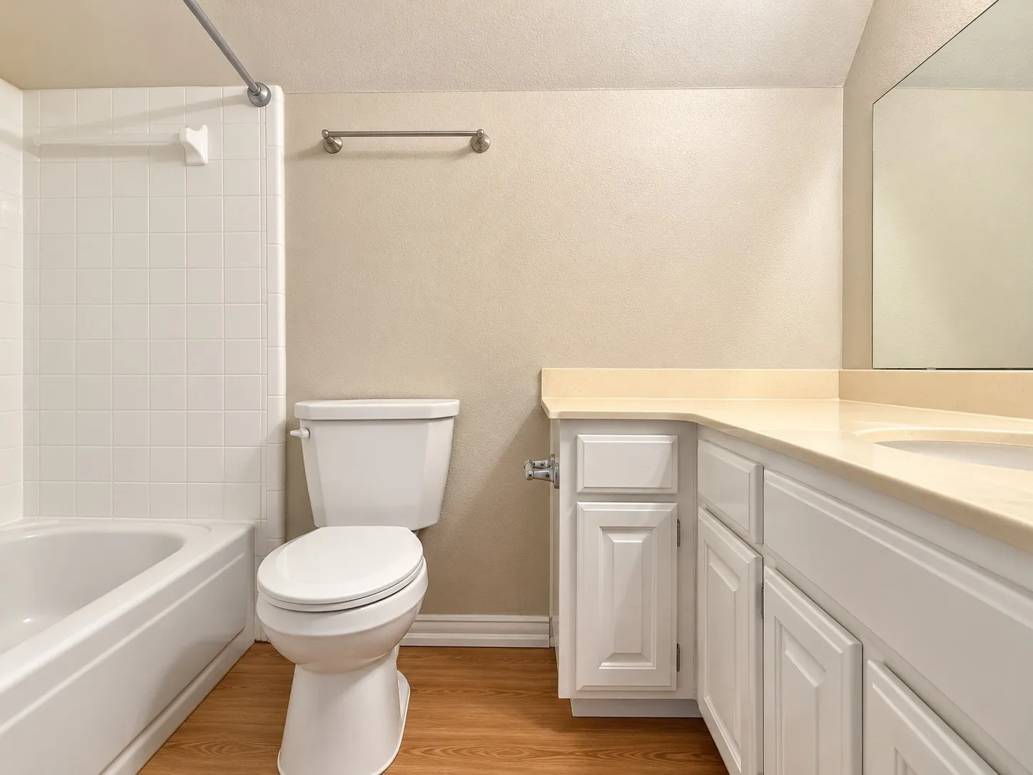 Bathroom featuring a vanity with white cabinetry and a solid-surface countertop, an integrated sink, a full-width wall mirror, wood-finish flooring, and a tub-shower combination with tile surround