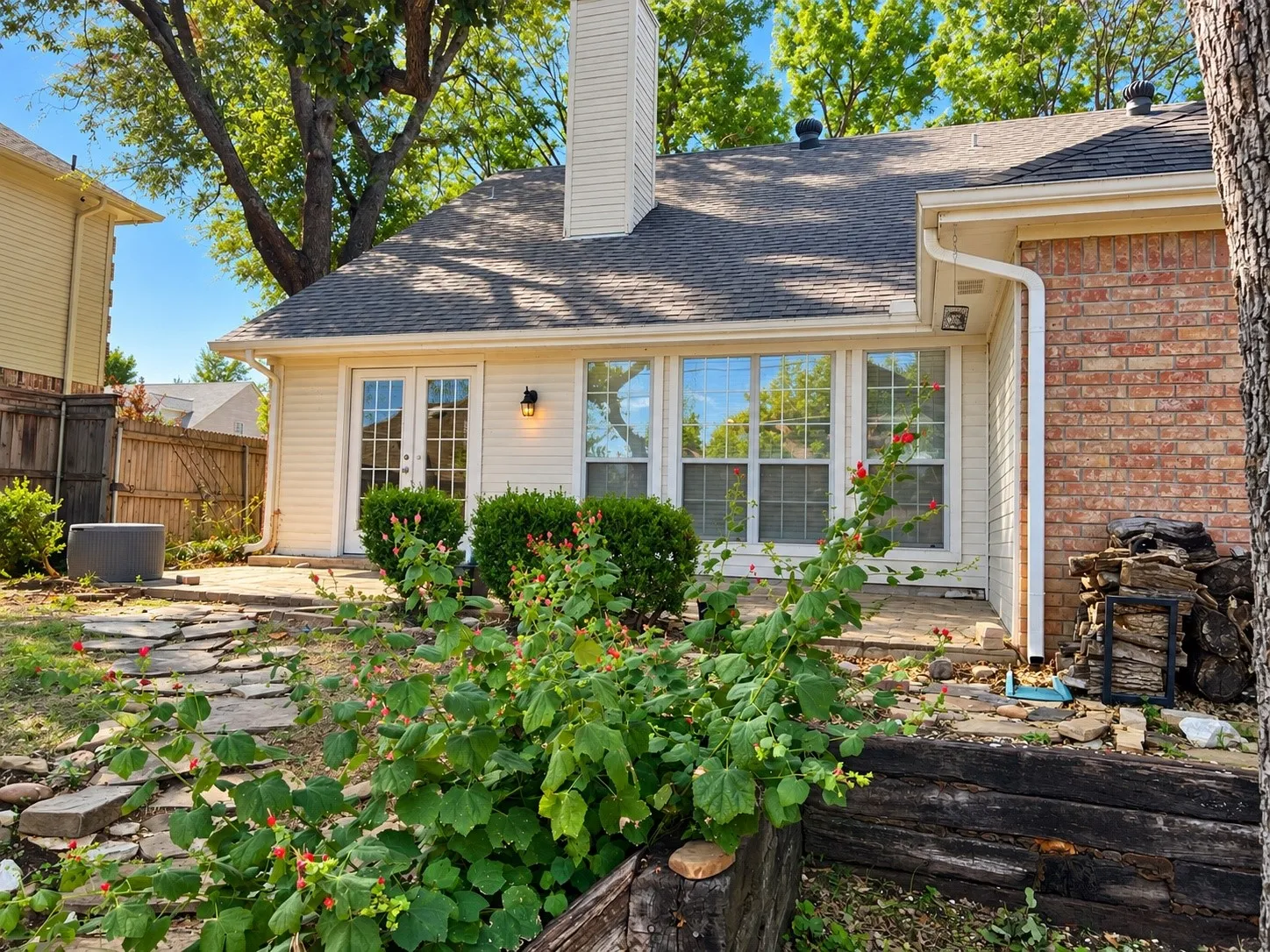 Exterior featuring a brick and siding facade, stone patio, prominent chimney, and French doors
