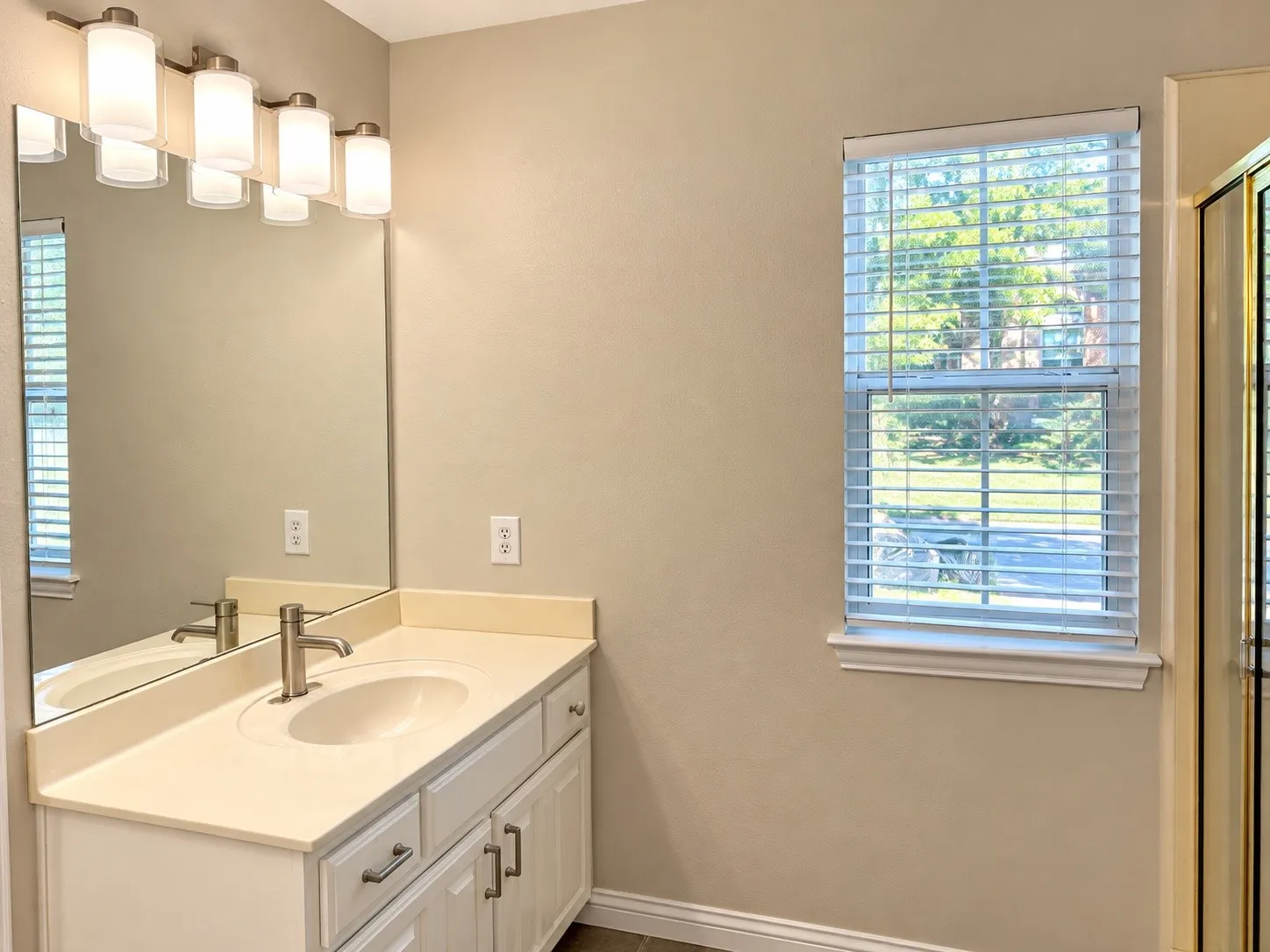 Bathroom vanity featuring a solid-surface countertop with an integrated oval sink, white cabinetry with brushed-metal pulls, a large wall-mounted mirror, and a five-light vanity fixture