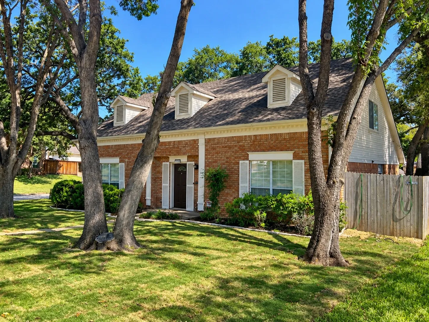 Brick exterior featuring a gabled roofline, three dormer windows, shuttered window accents, and mature shade trees